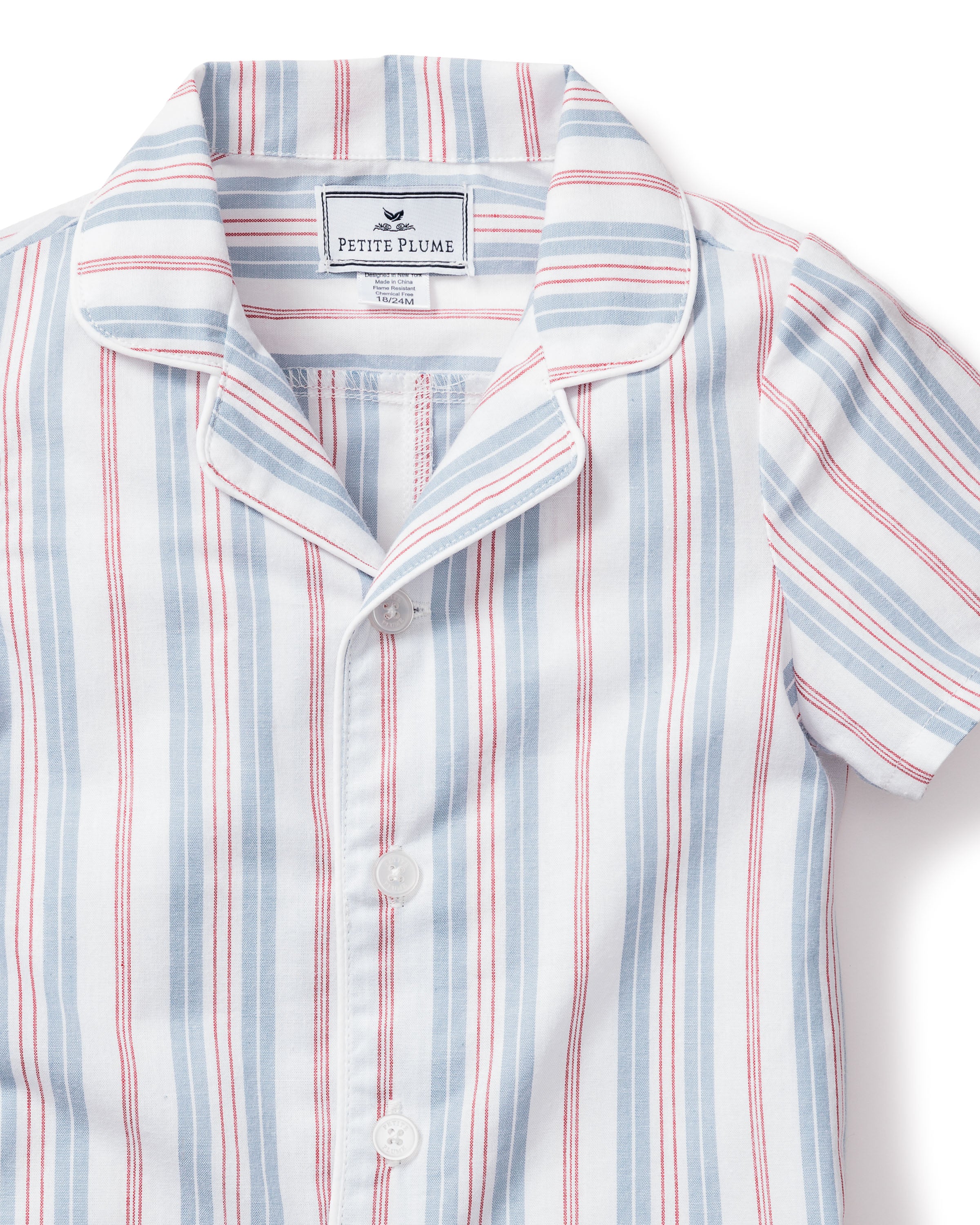 A short-sleeved button-up collar shirt with red and blue vintage stripes on white, labeled Petite Plume, evokes timeless charm.