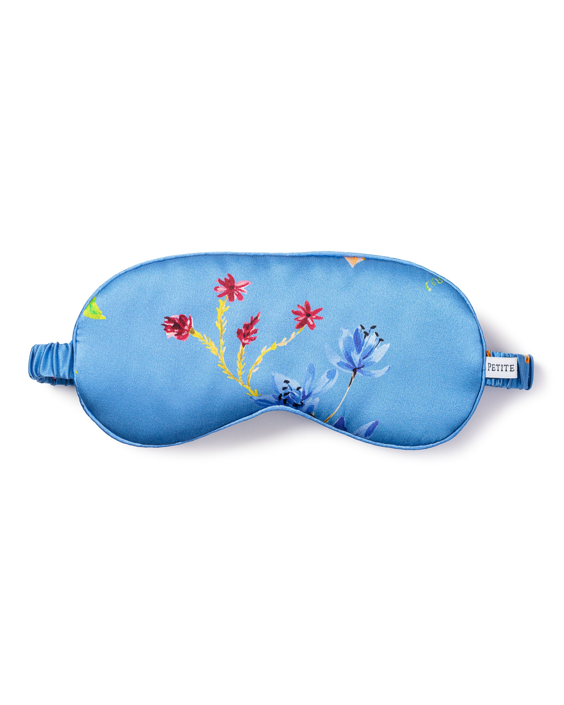 The Womens Silk Sleep Mask in Azure Brilliant Botanical by Petite Plume is a luxurious blue mask made from pure silk, featuring an adjustable strap and a botanical garden print with red and blue flowers, complete with a small side tag.