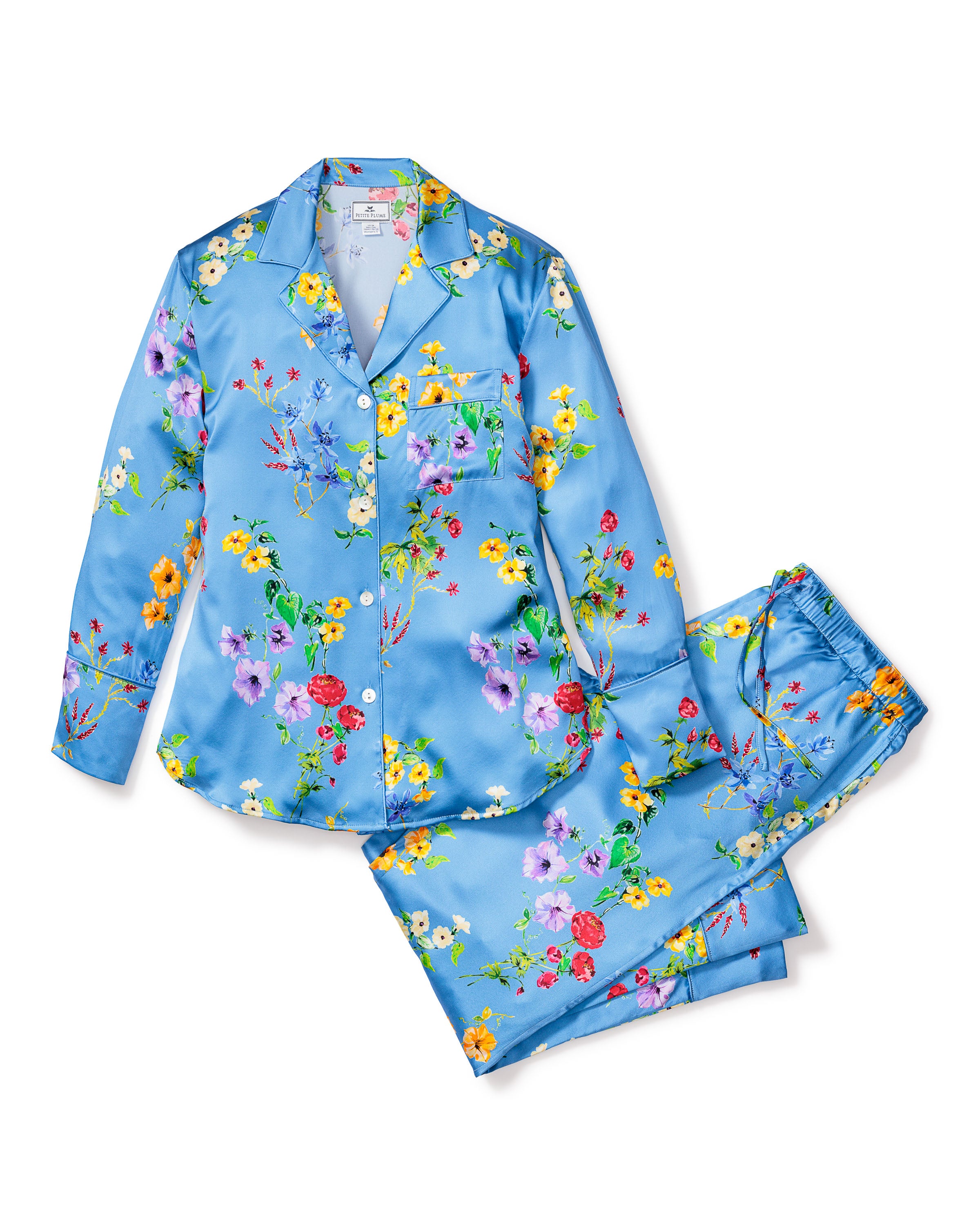 The Petite Plume Womens Silk Pajama Set in Brilliant Botanical Azure features a long-sleeve button-down top and elastic waistband pants, adorned with vibrant colorful flowers on luxurious blue satin.