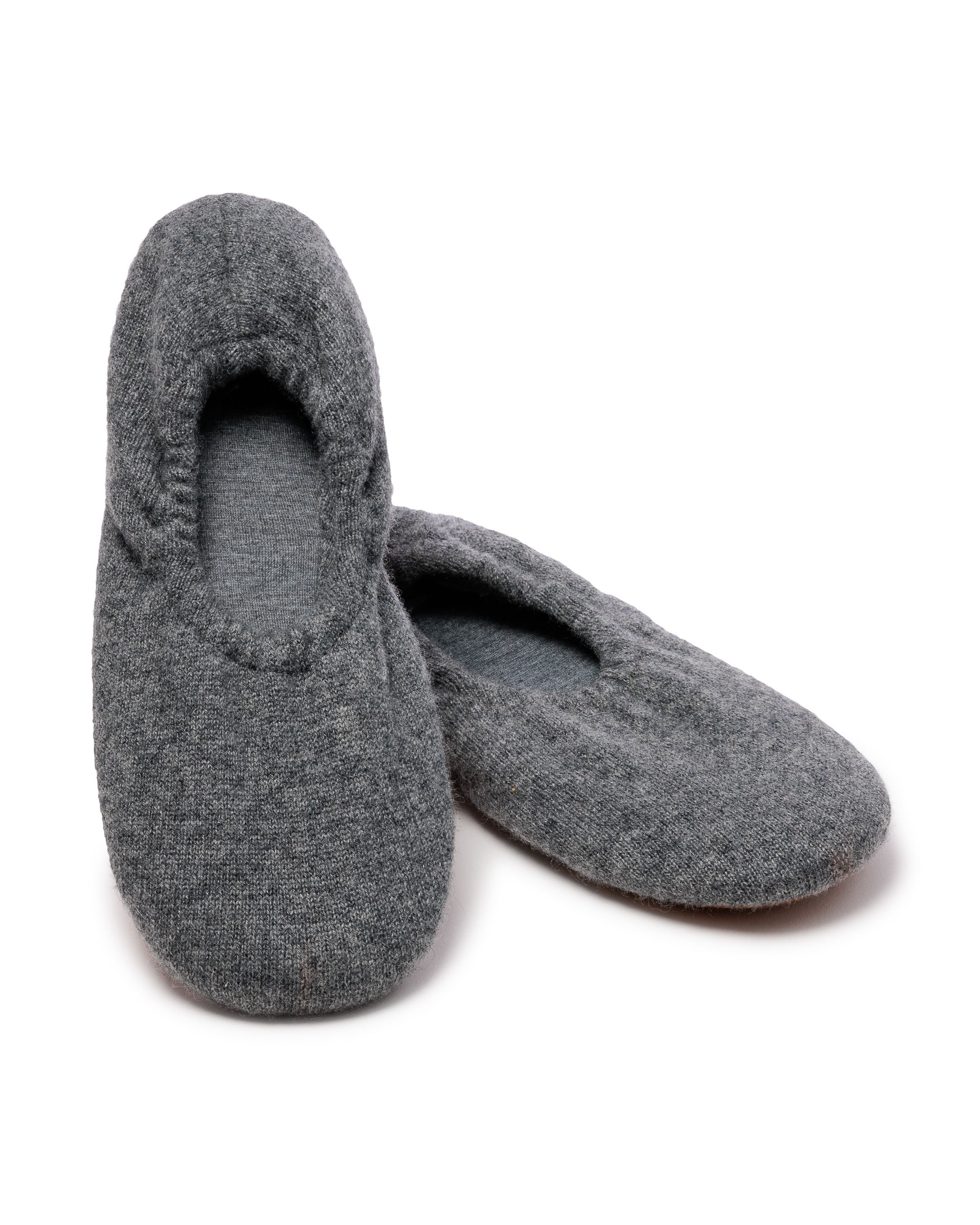 Petite Plumes Womens Cashmere Slippers in Dark Grey are made from 100% cashmere with a cozy fit design, a closed toe, and an elasticized opening. Displayed on a white background, one slipper is slightly in front of the other.