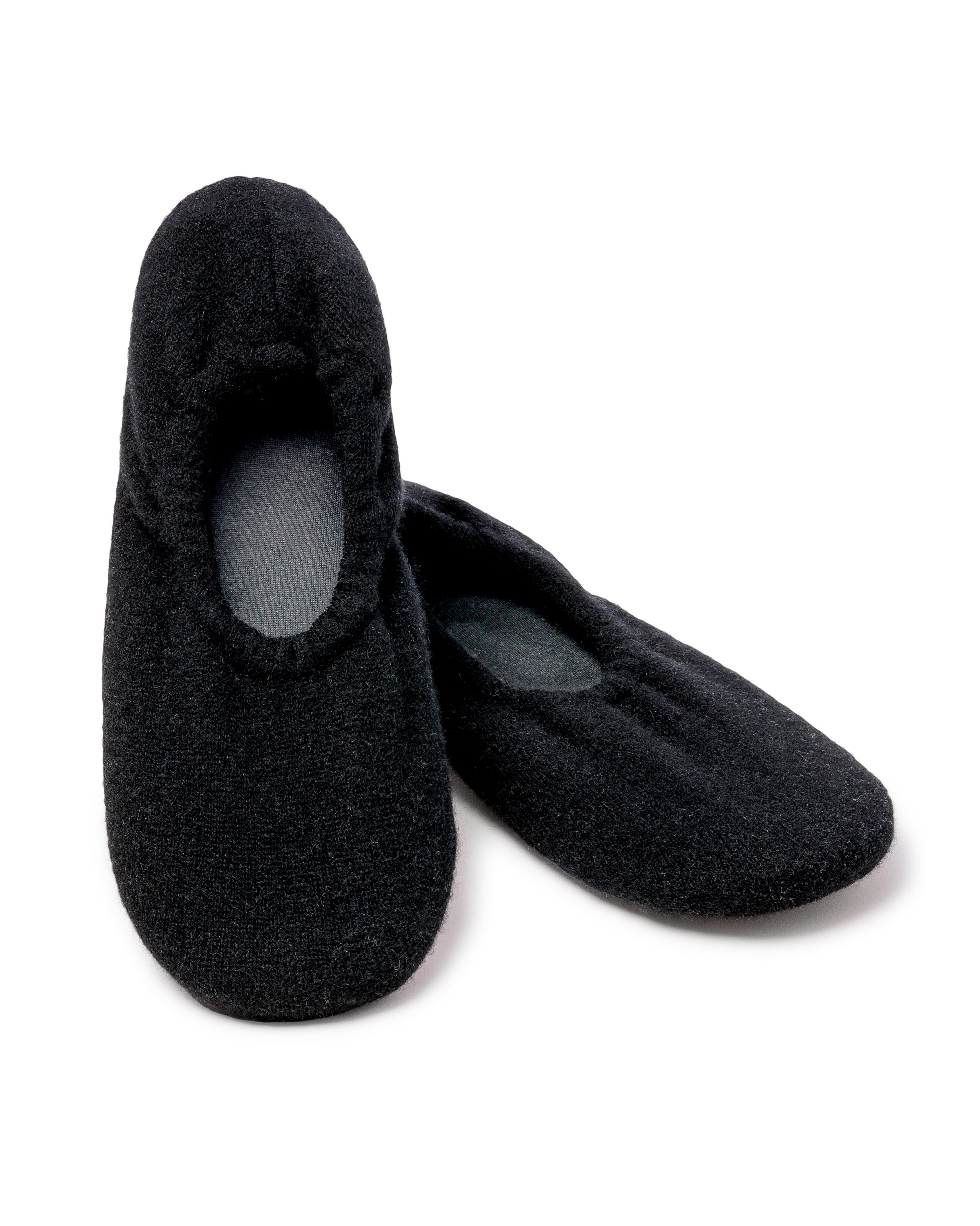 The Petite Plume Womens Cashmere Slippers in Black feature a simple, cozy design with a slightly padded interior and rounded toe. One slipper stands upright while the other leans against it, showcasing their perfect fit.