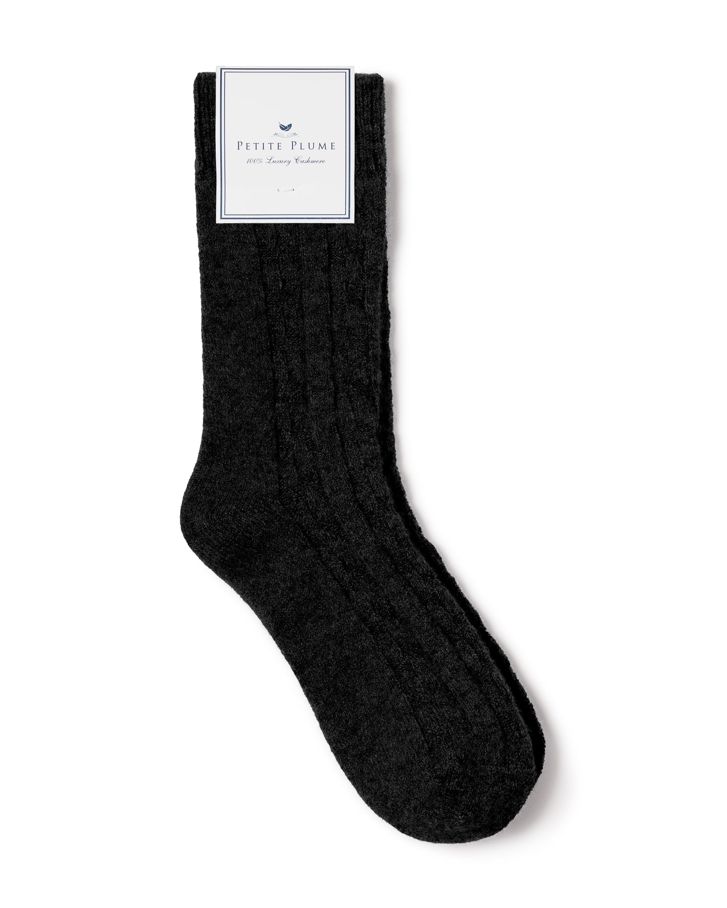 A single black ribbed sock features a white label with the brand name Petite Plume and boasts 100% Grade A Cashmere, positioned on a plain white background, representing luxurious comfort.