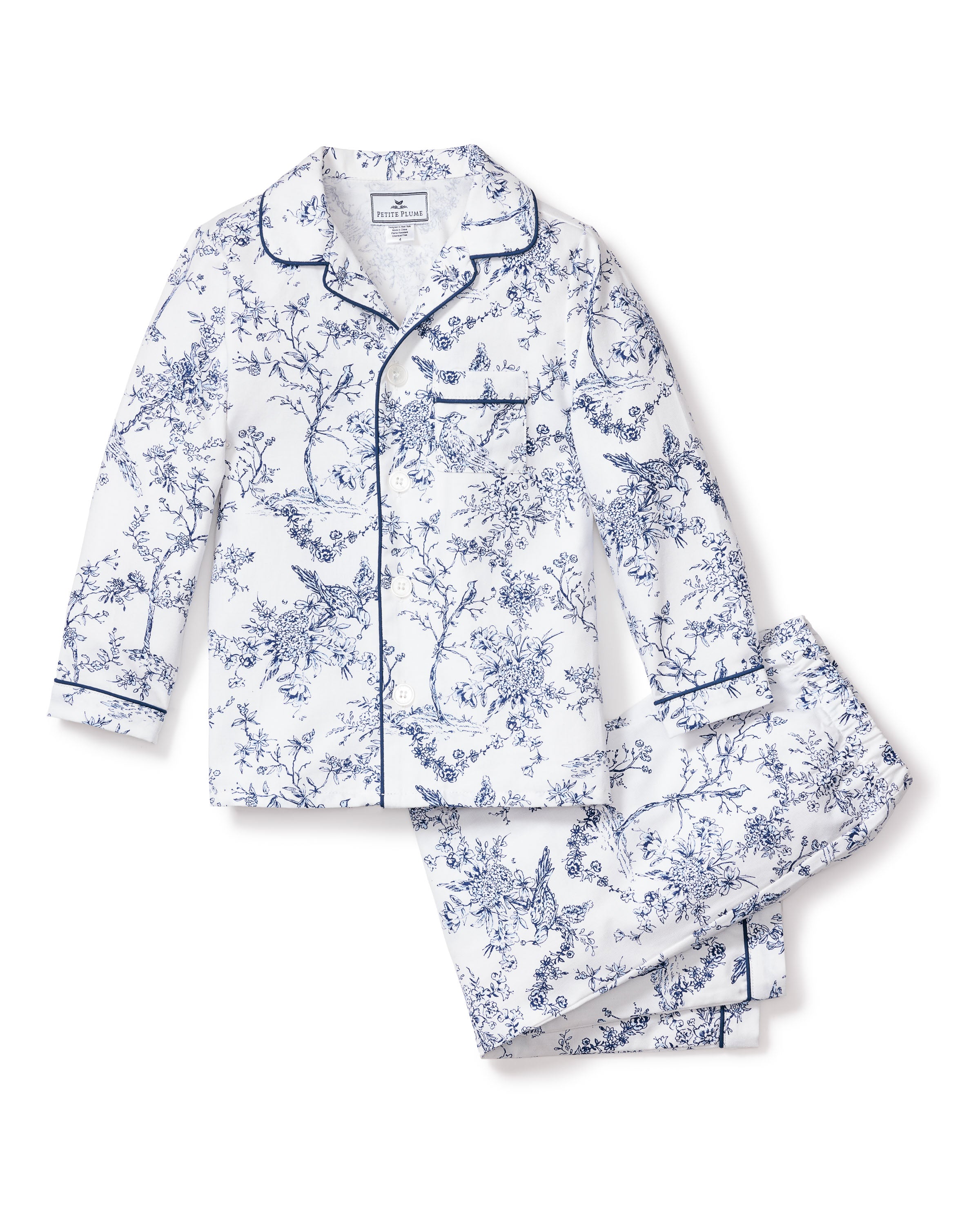 The Kids Twill Pajama Set in Timeless Toile by Petite Plume features a long-sleeve, luxury sleepwear style with a classic collar and matching pants. Its white background showcases an intricate blue floral and bird pattern for a vintage, sophisticated charm.