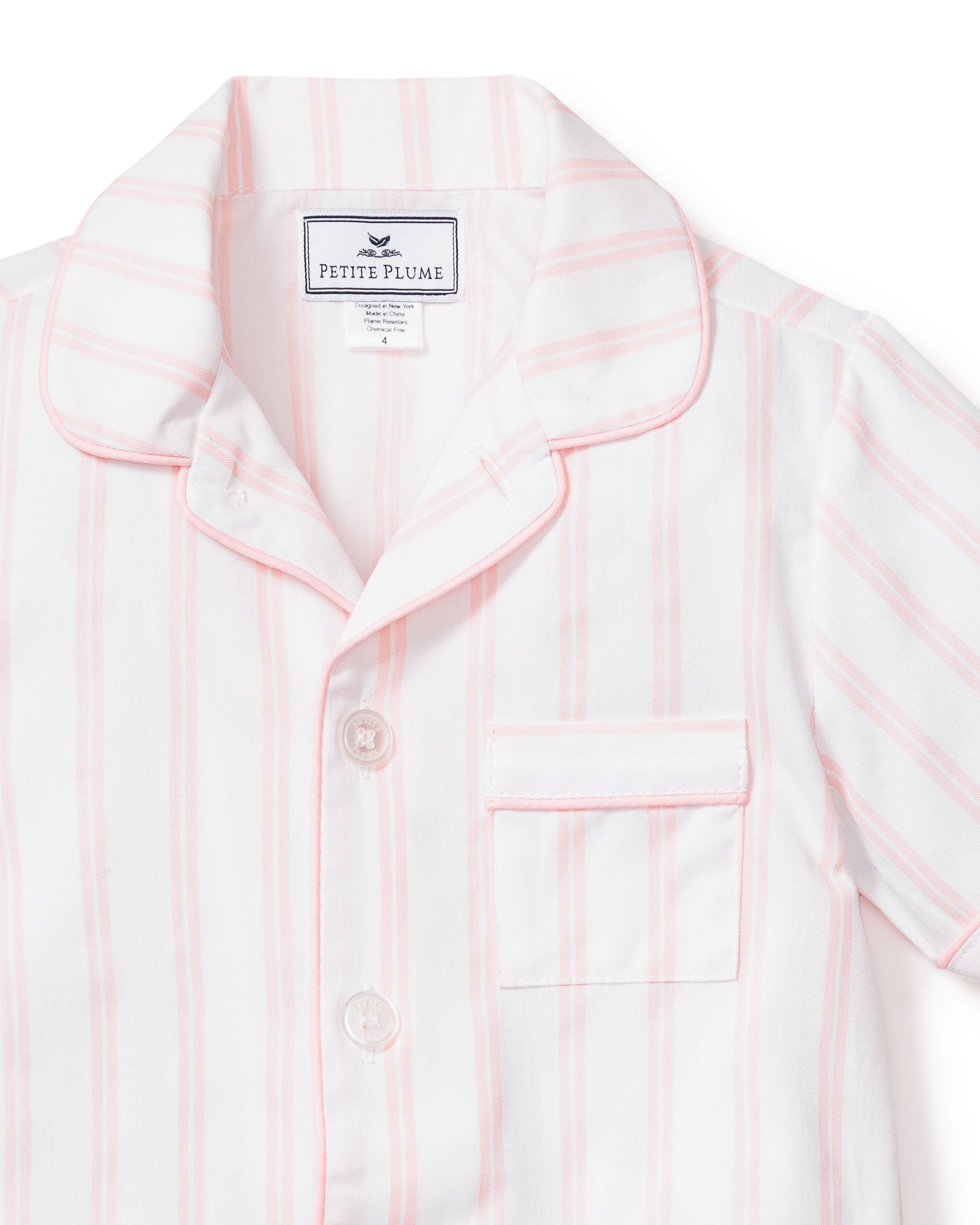 This luxurious sleepwear piece is a close-up of the Kids Twill Pajama Short Set in Pink and White Stripe by Petite Plume. It features a notched collar, button-down front, and chest pocket with Petite Plume on the label inside the collar.