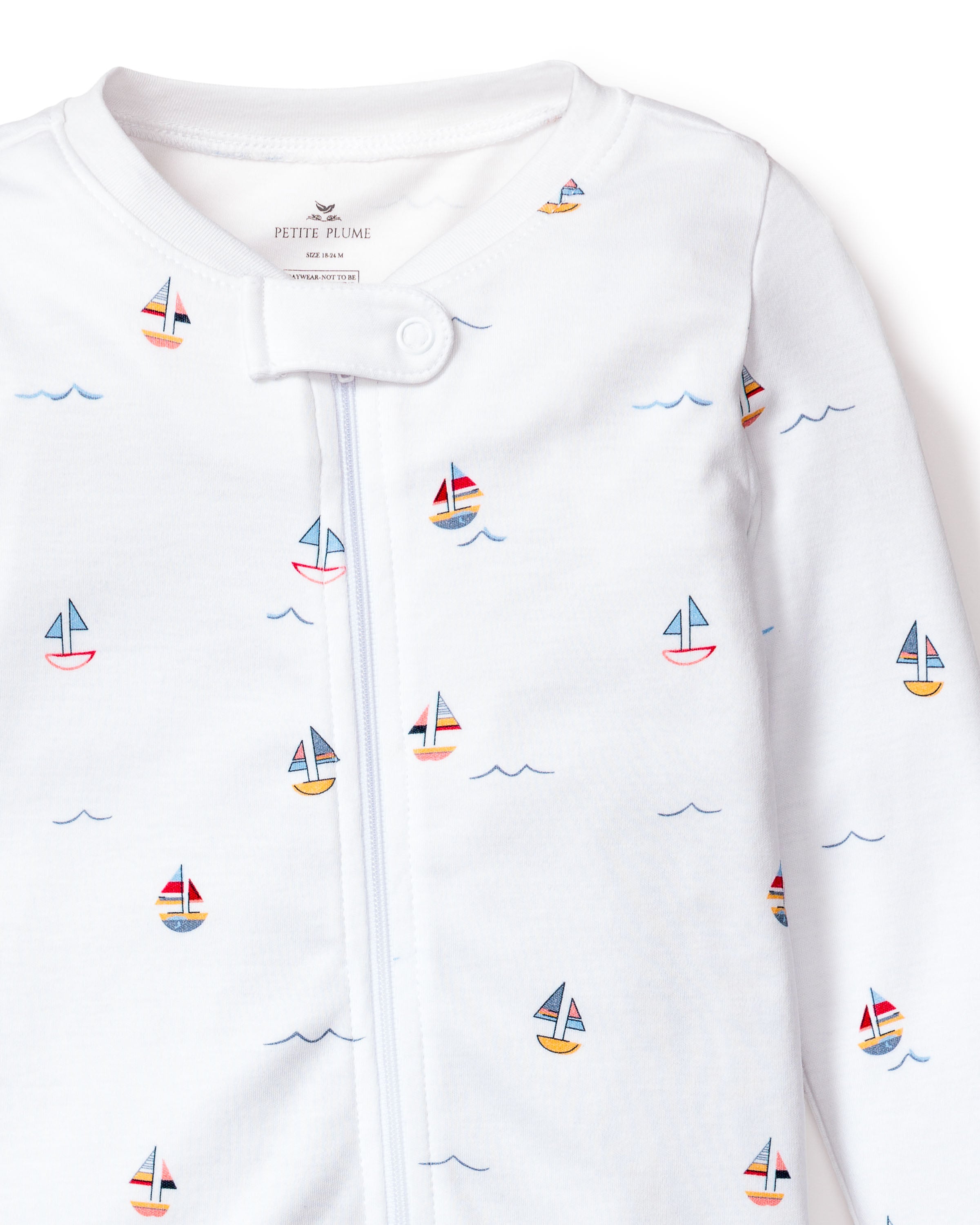 The Babys Pima Romper in Bateau by Petite Plume is a white onesie featuring colorful sailboat and blue wave designs. Made from soft Pima cotton, it ensures comfort with front fastening snaps.