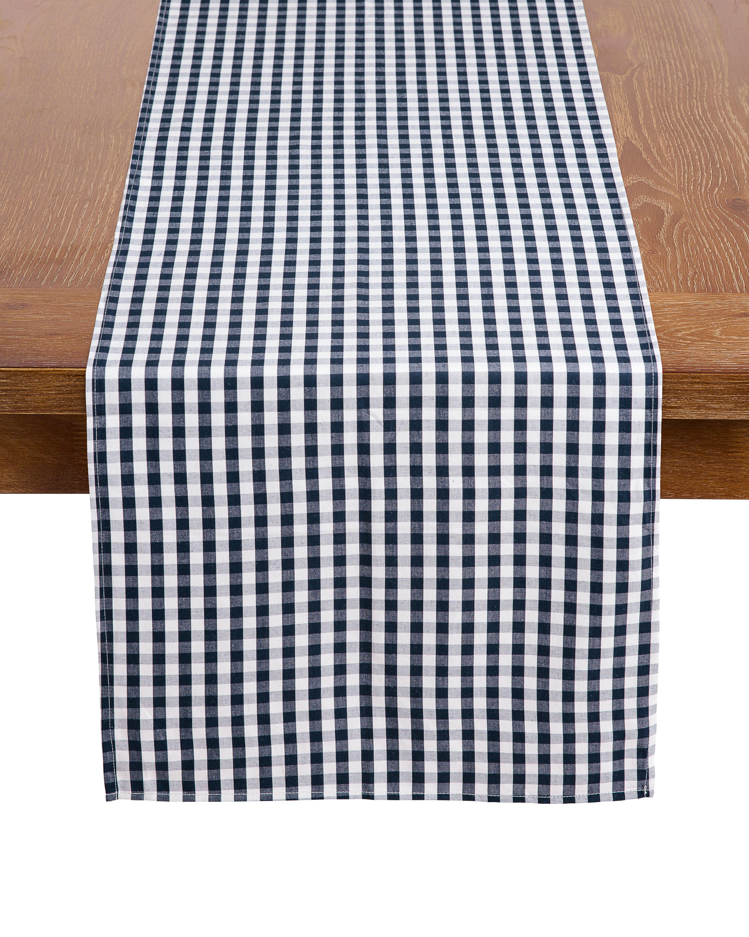 A wooden table with Petite Plumes Signature Twill Table Runner in Navy Gingham drapes over the center. The 100% cotton features alternating squares, adding a classic touch to this festive tablescape.