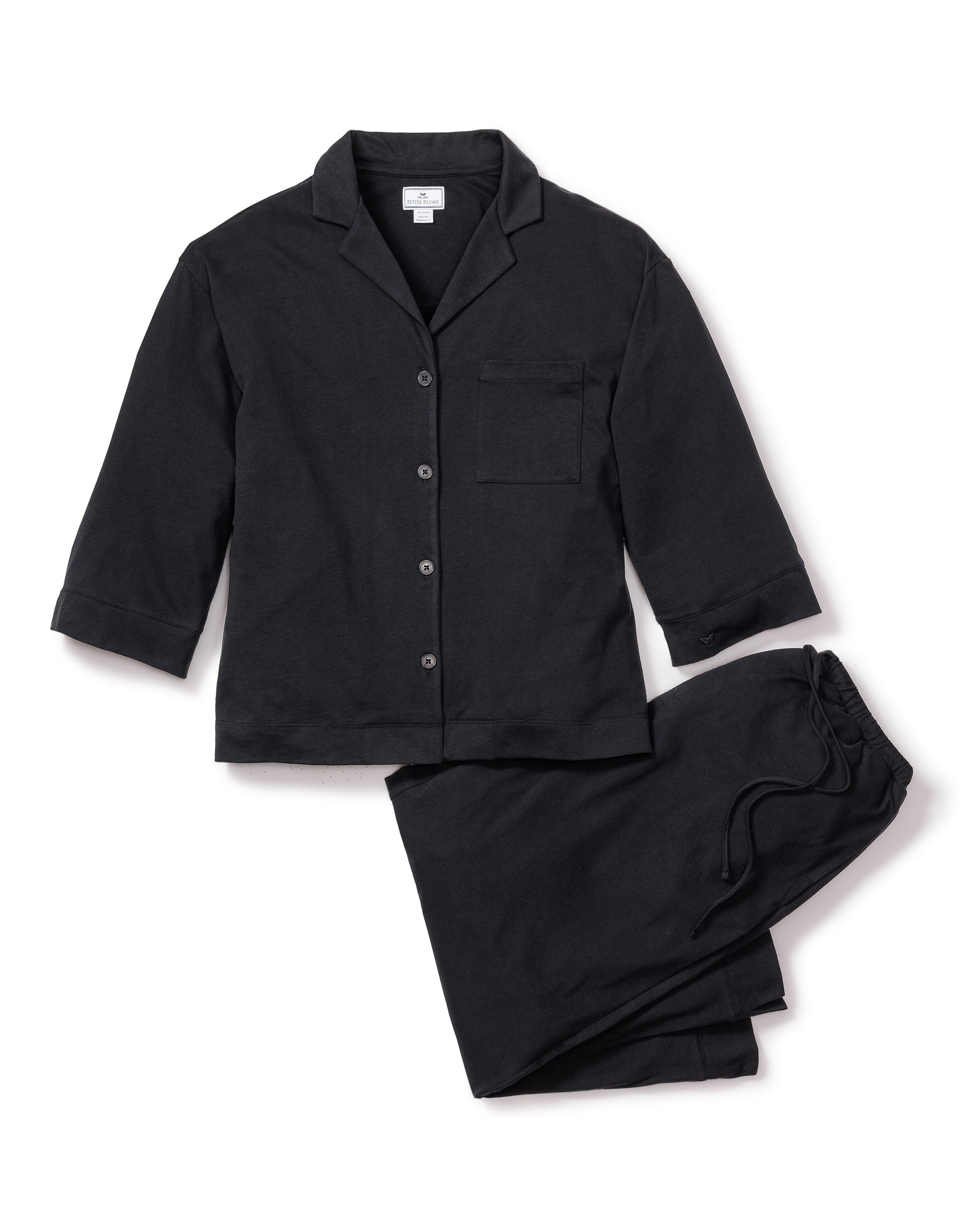 The Olivia Wide Leg Pima Pajama Set in Black by Petite Plume is a luxurious Peruvian Pima cotton ensemble with a long-sleeve button-up top featuring a chest pocket and matching drawstring pants. The set, displayed on a plain white background, highlights its elegant jersey knit finish.