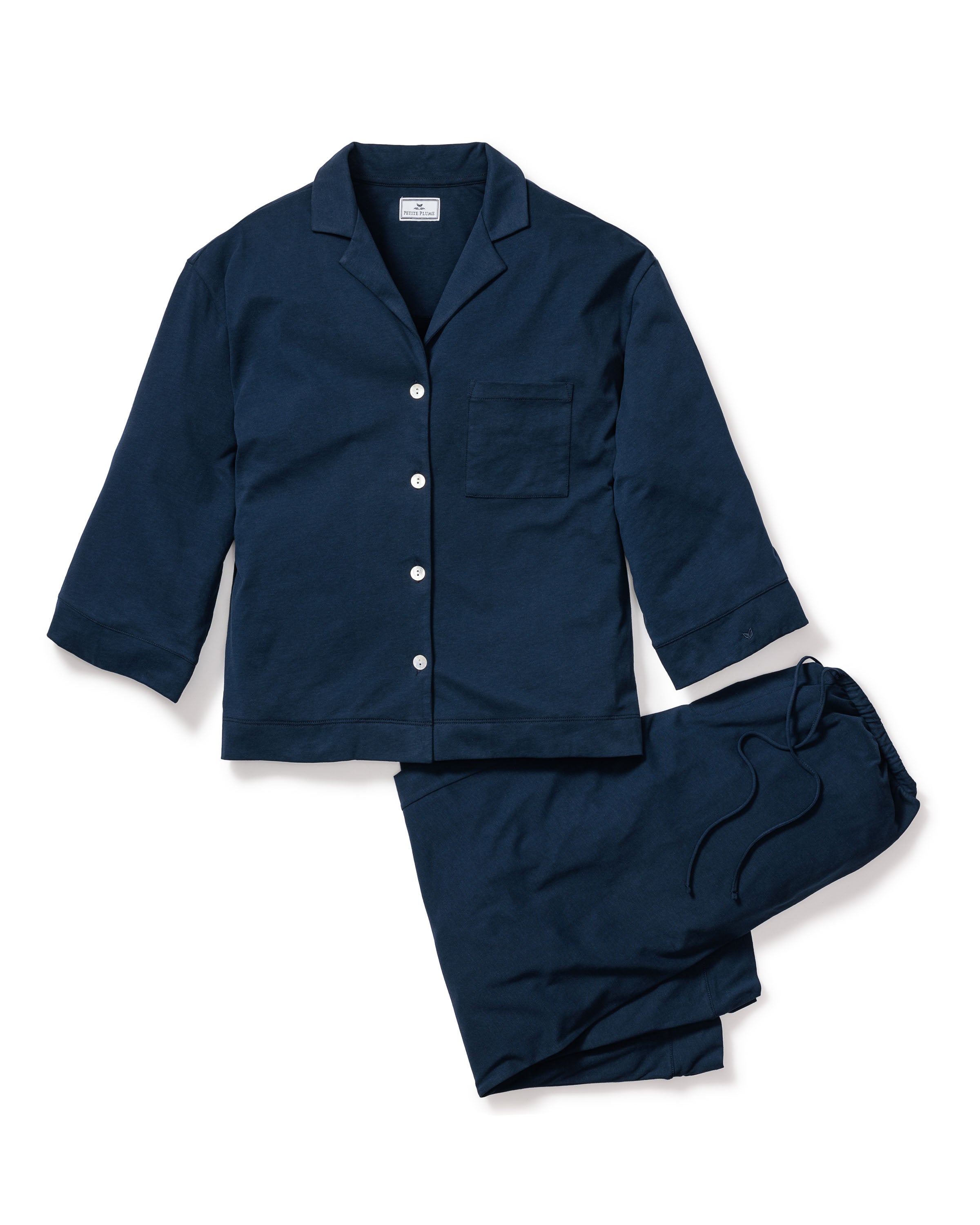 The Olivia Wide Leg Pima Pajama Set in Navy by Petite Plume is a luxurious jersey knit ensemble made of soft Pima cotton, including a button-up long-sleeve top with a chest pocket and matching drawstring pants, presented against a white background.