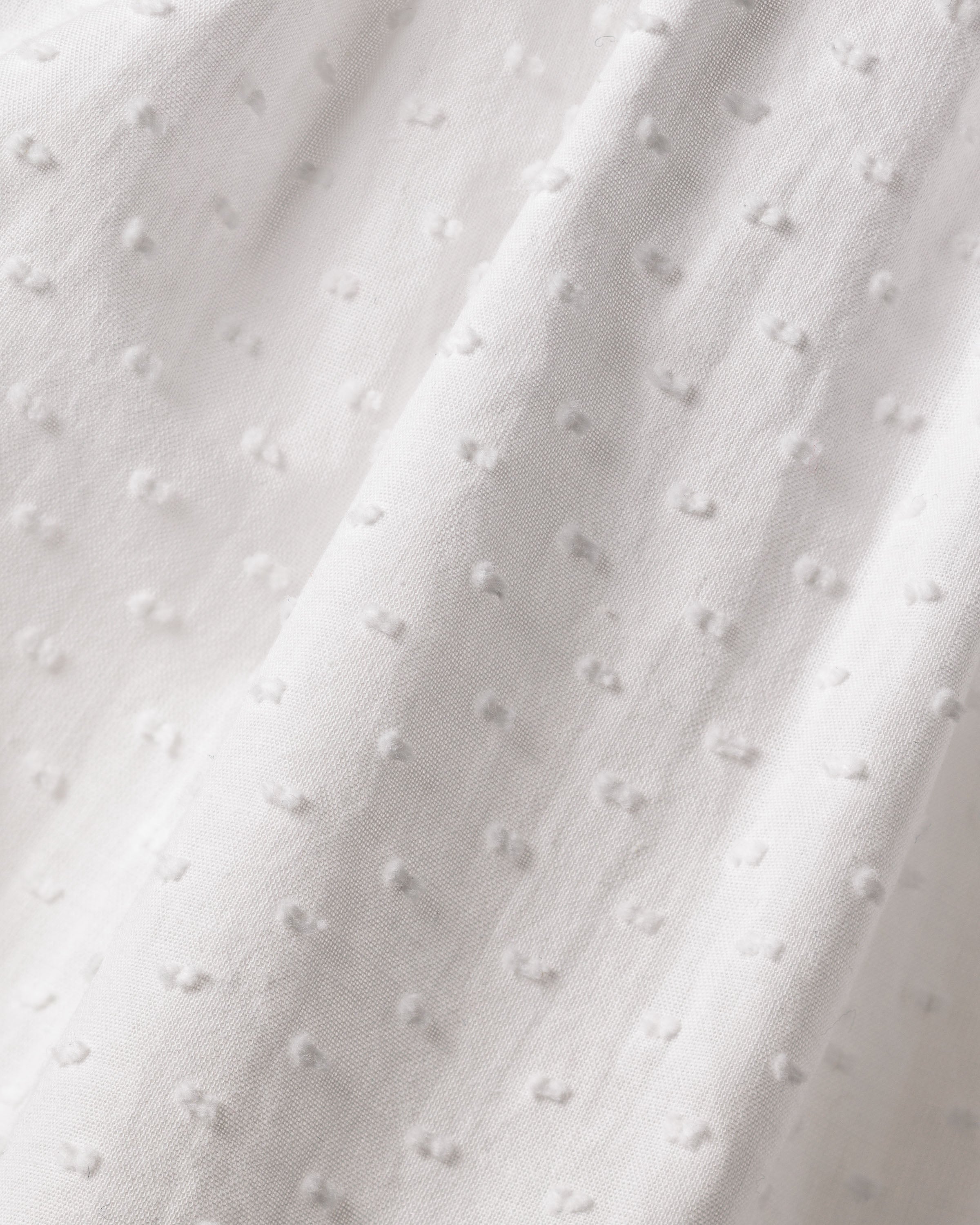 Close-up view of the Girls Swiss Dots Serene Day Dress in White by Petite Plume, made from fabric featuring small raised dot patterns for a textured and delicate look, ideal for luxury sleepwear.