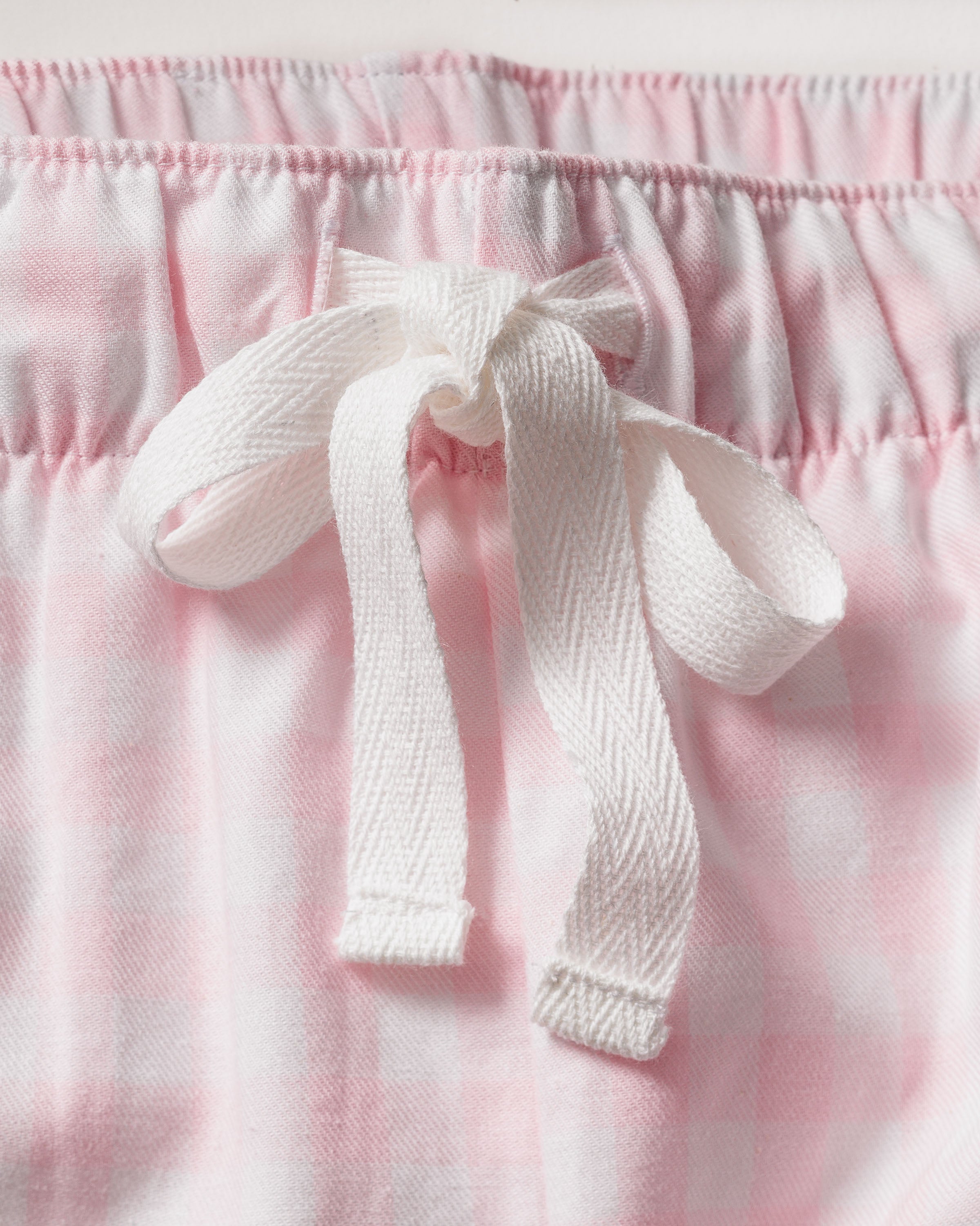 A close-up of the Womens Twill Pajama Short Set in Pink Gingham by Petite Plume shows a soft pink and white gingham fabric, elastic waistband, and tied white drawstring bow, epitomizing luxurious sleepwear.