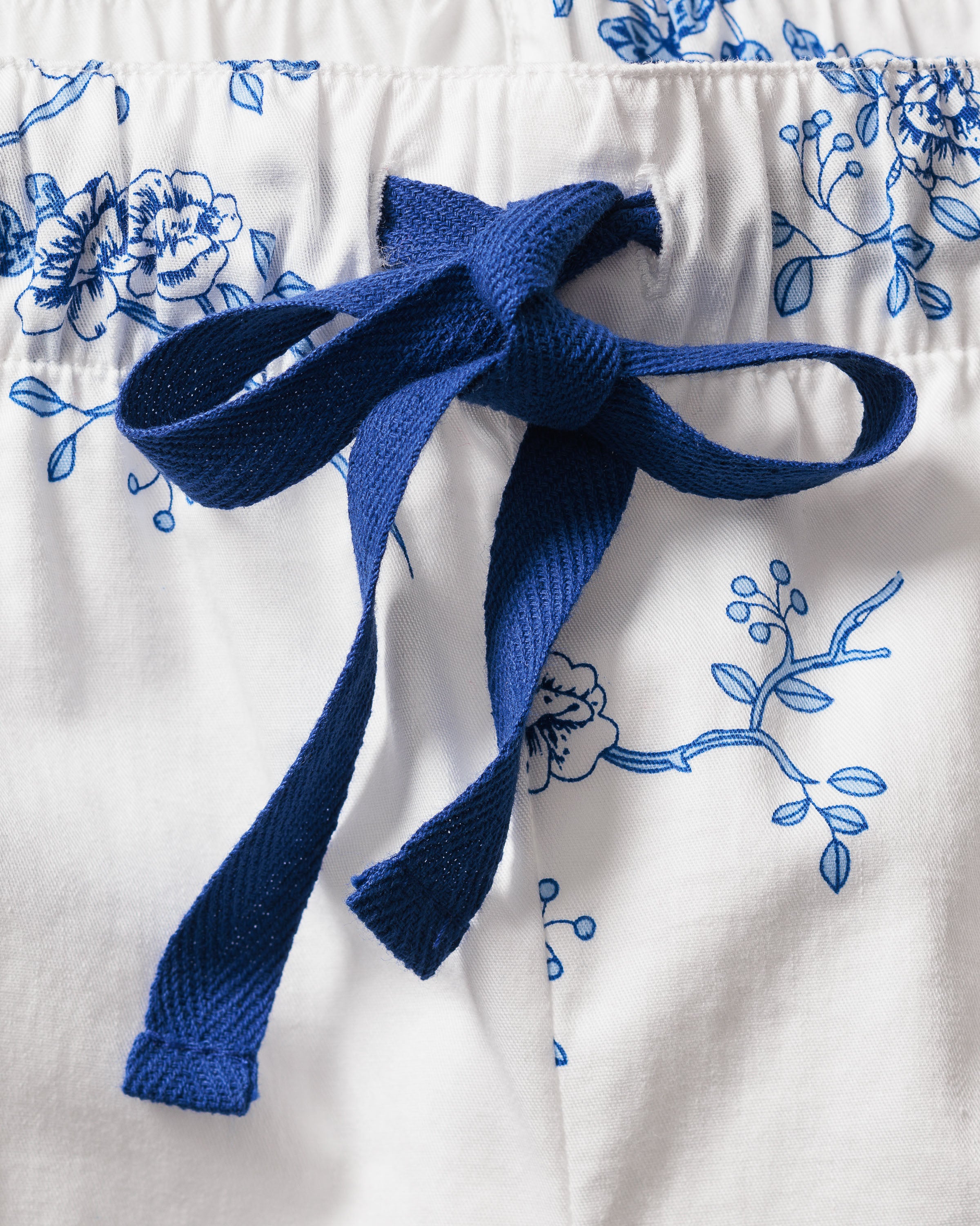 Close-up of womens white twill pajama shorts in indigo floral by Petite Plume, crafted from top-quality cotton with a blue bow-tied fabric drawstring.