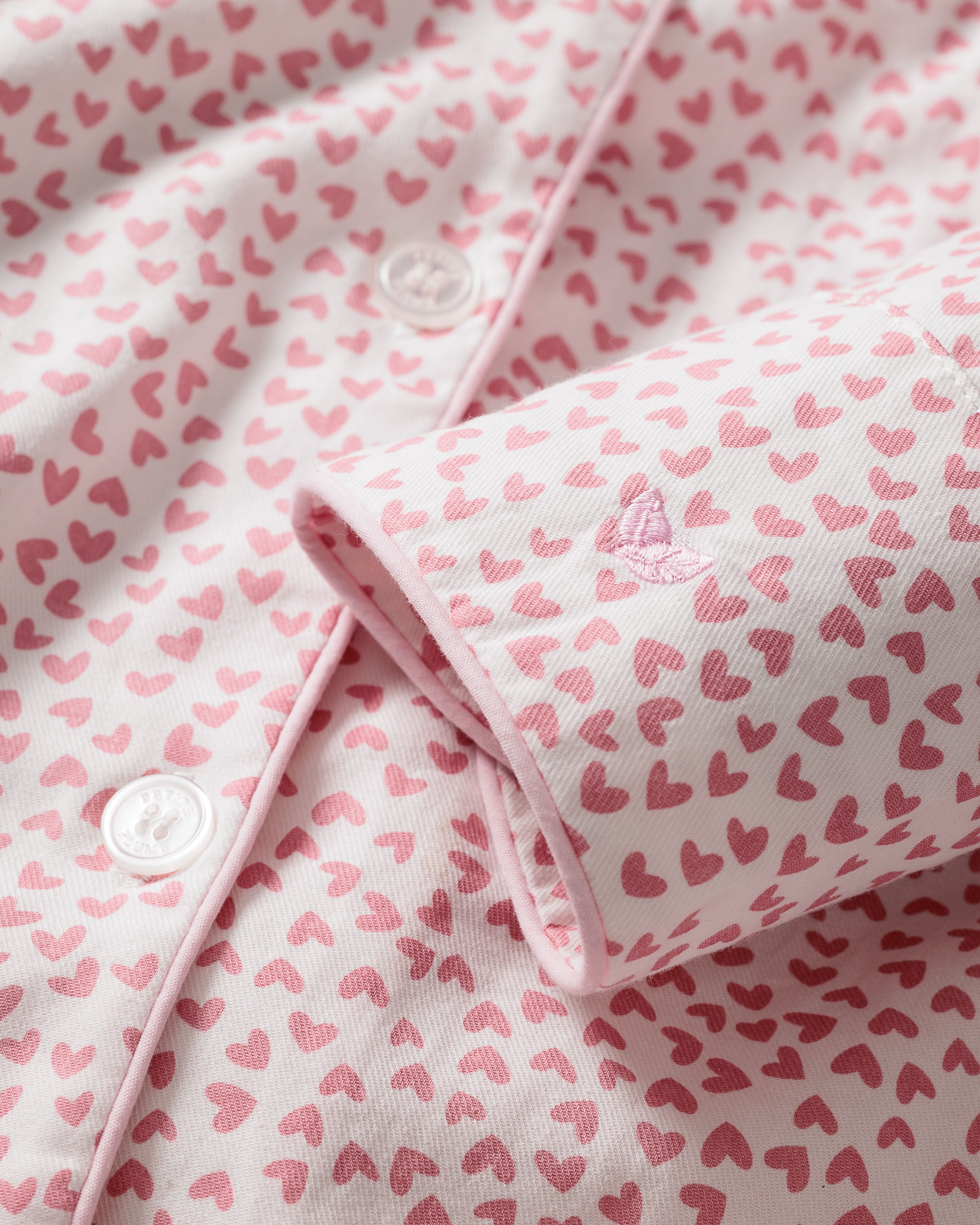 Close-up of Petite Plumes Womens Twill Nightshirt in Sweethearts: soft luxury sleepwear fabric with a pink and white heart pattern, white edge buttons, folded cuff with small embroidery—the delicate, playful design perfect for elegant nightwear.