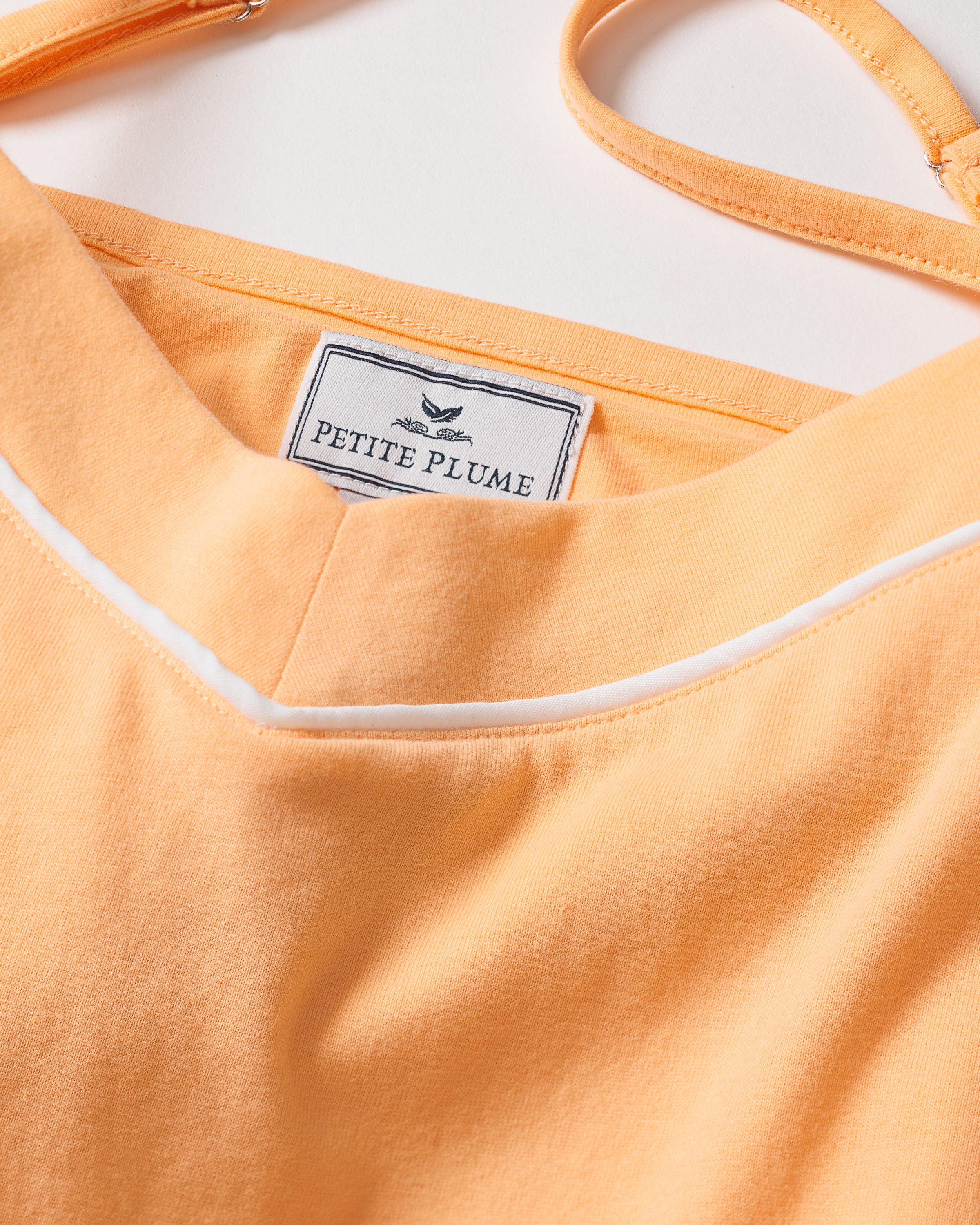 Close-up of a peach cami and short set with white piping on the neckline, crafted from soft Pima cotton. The tag inside reads Petite Plume with a small logo, indicating its part of a buttery pajama set designed for ultimate comfort.