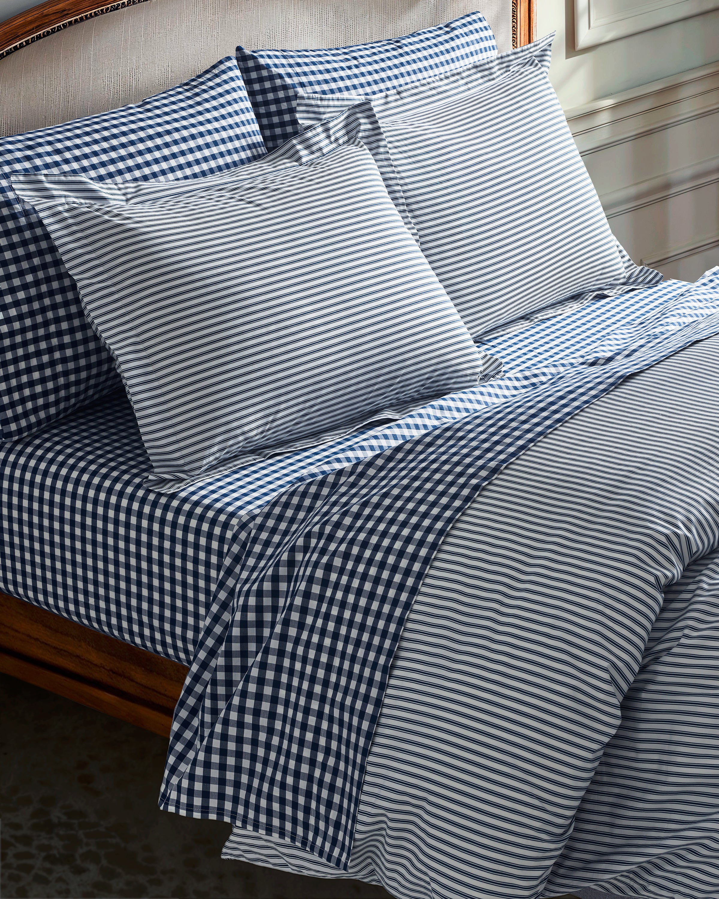 A neatly made bed with the Luxe Premium Percale Duvet Set in Navy French Ticking by Petite Plume, featuring blue and white striped and checkered luxury sheets. The set includes pillows, creating a cozy and inviting look in a well-lit room.