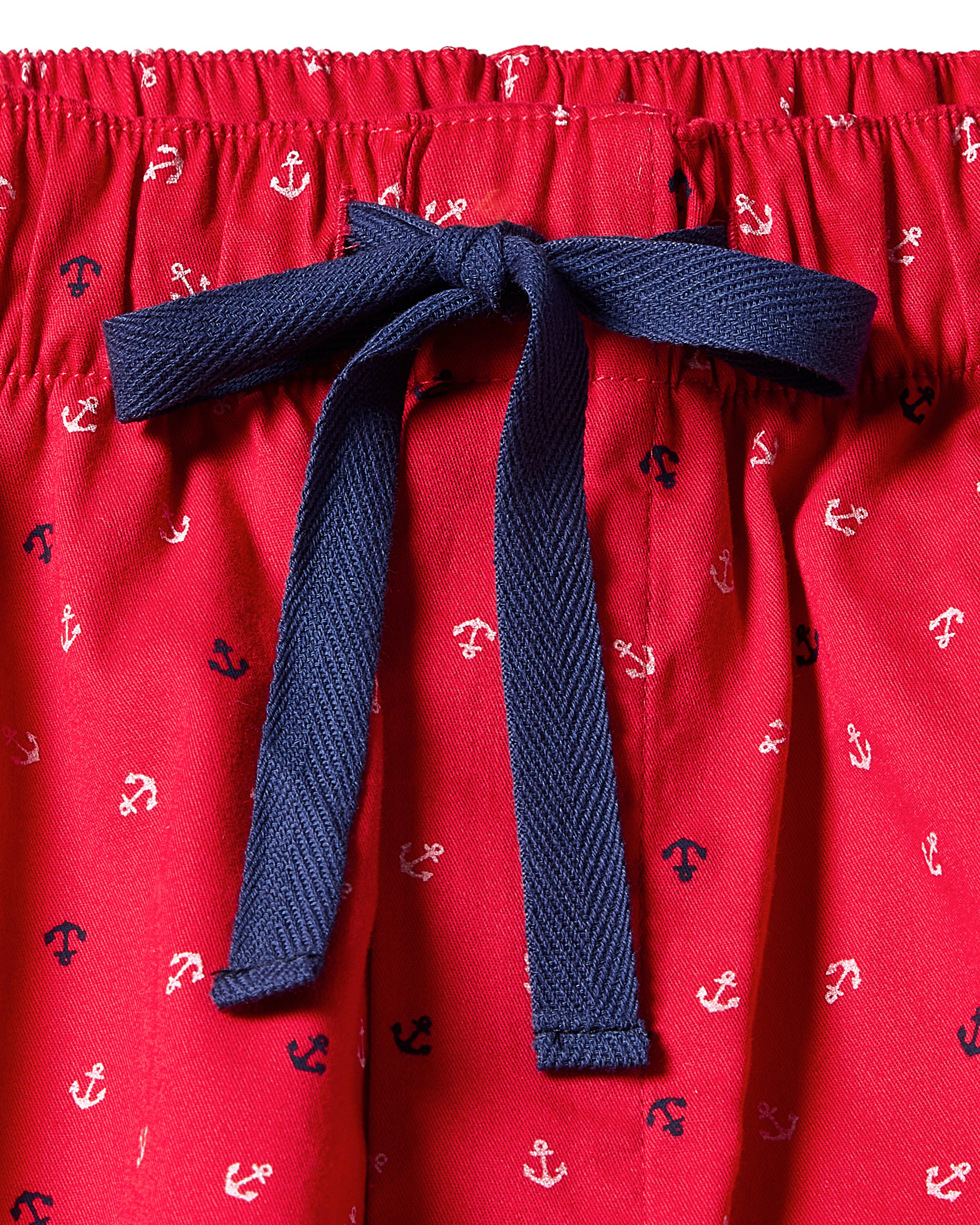 Close-up of Mens Twill Pajama Pant in Anchors Away by Petite Plume, showcasing a red design with small navy and white anchors. Crafted from premium cotton, these yarn-dyed pants feature a blue drawstring bow at the waist.