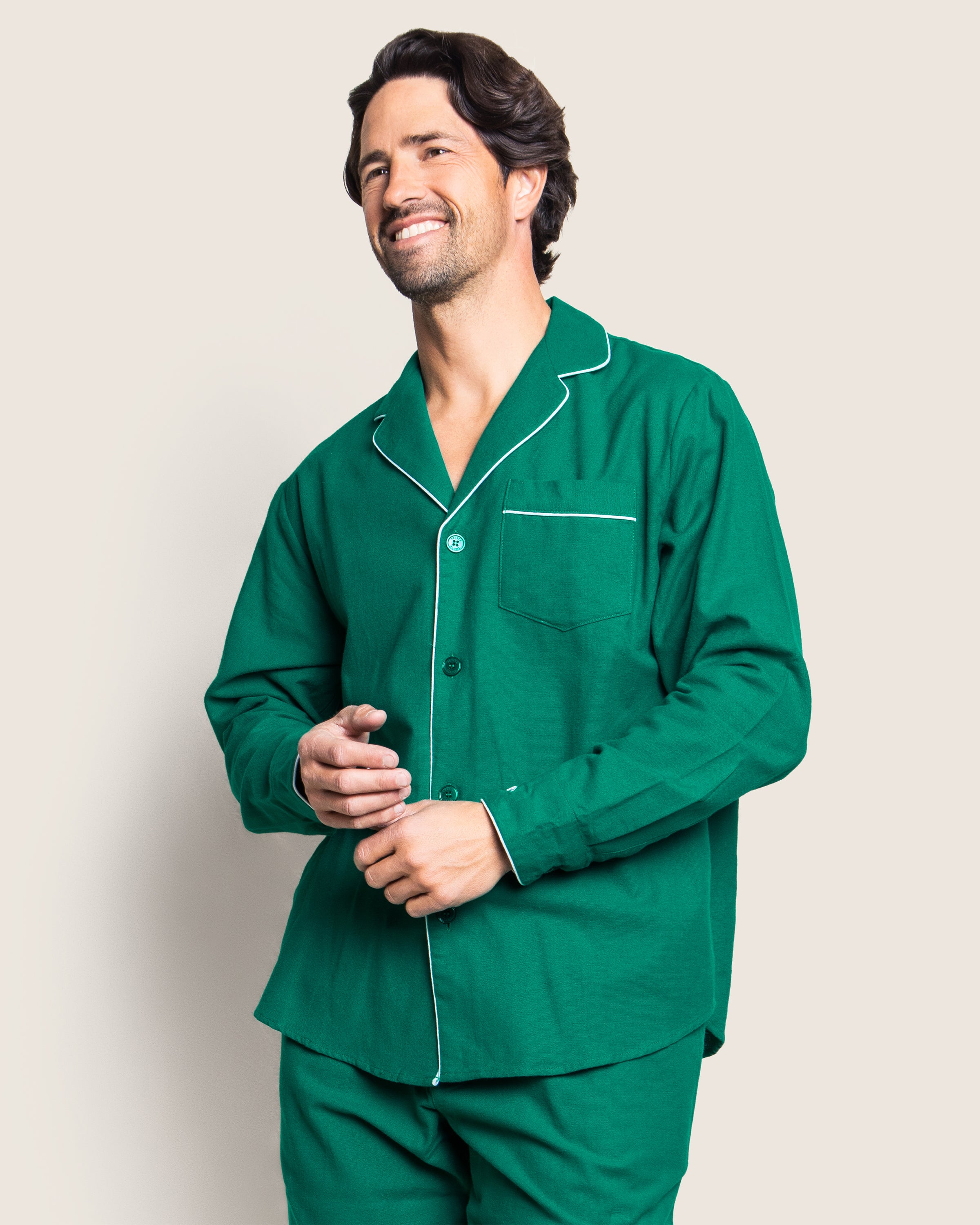 A person smiles while wearing Petite Plumes Mens Flannel Pajama Set in Forest Green, standing against a plain, light-colored background.