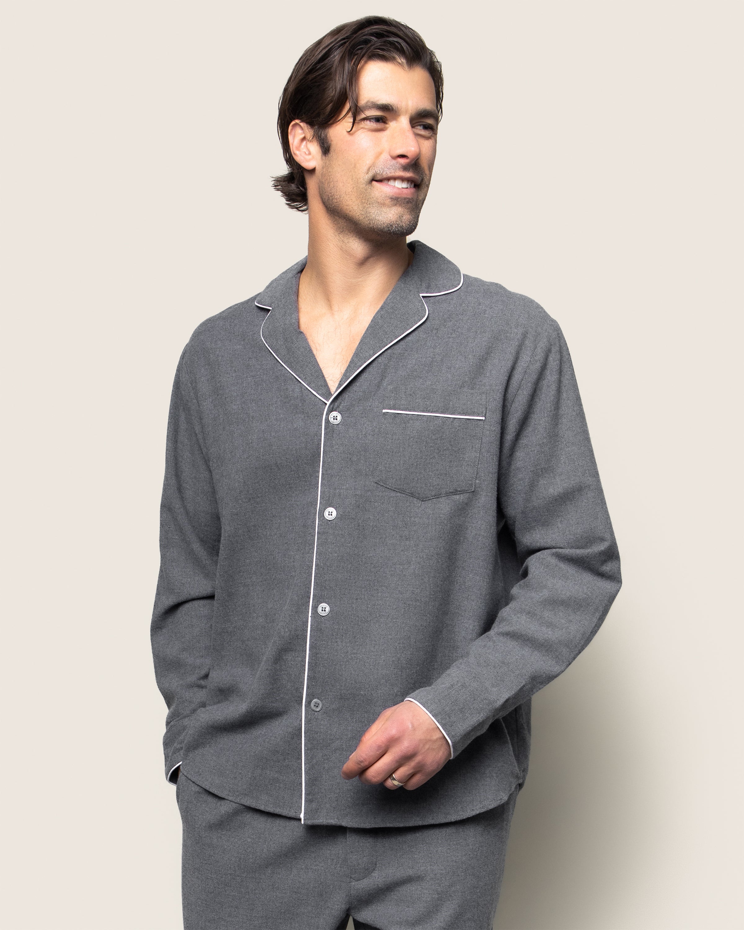 A person smiles with one hand in their pocket, wearing the Petite Plume Mens Flannel Pajama Set in Grey against a light gray background, enjoying the comfort of their moisture-wicking attire.