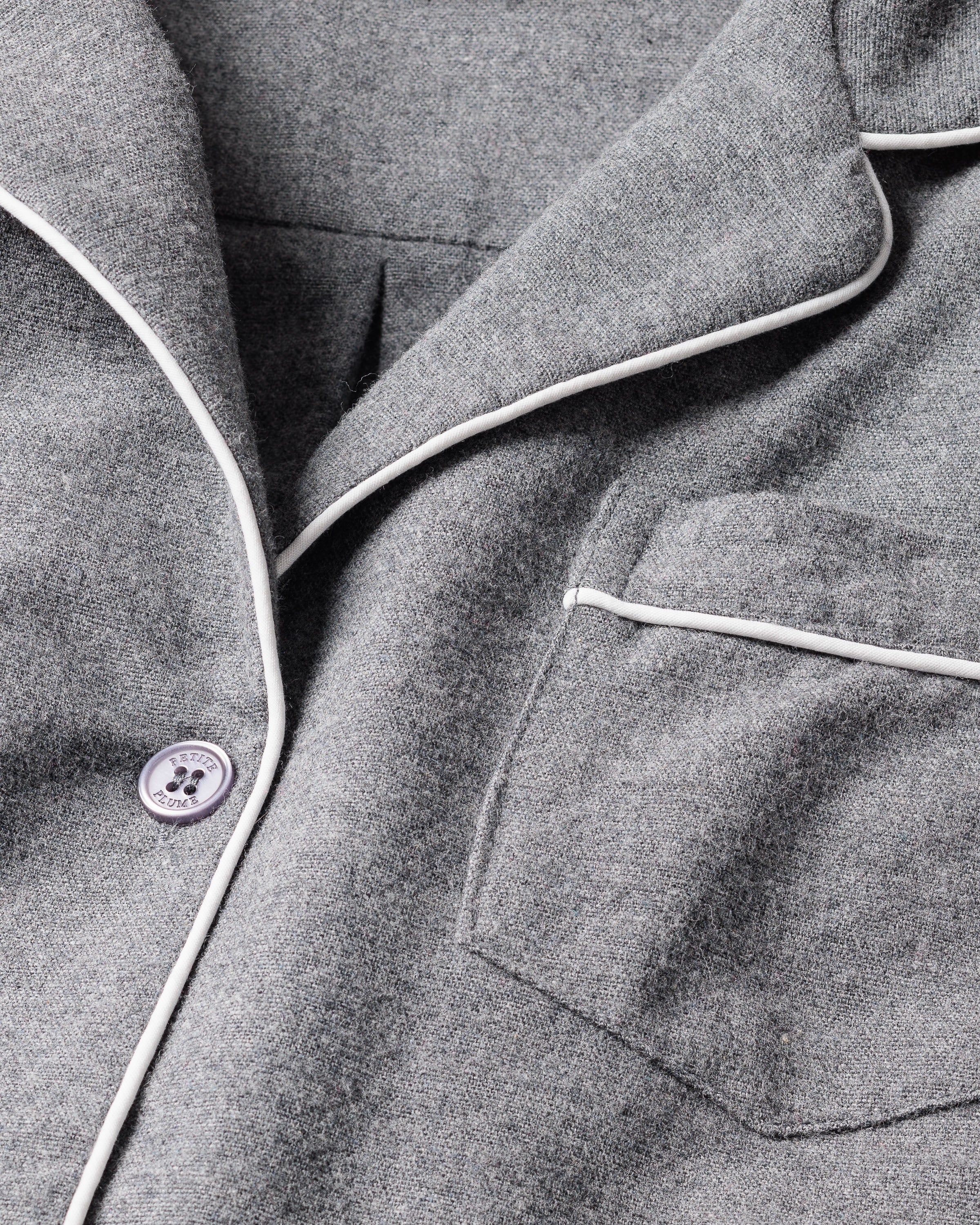 Close-up of a gray flannel fabric jacket from the Mens Flannel Pajama Set by Petite Plume. It features a single button, white piping on the edges, a chest pocket with matching trim, and offers a soft textured look for moisture-wicking comfort.