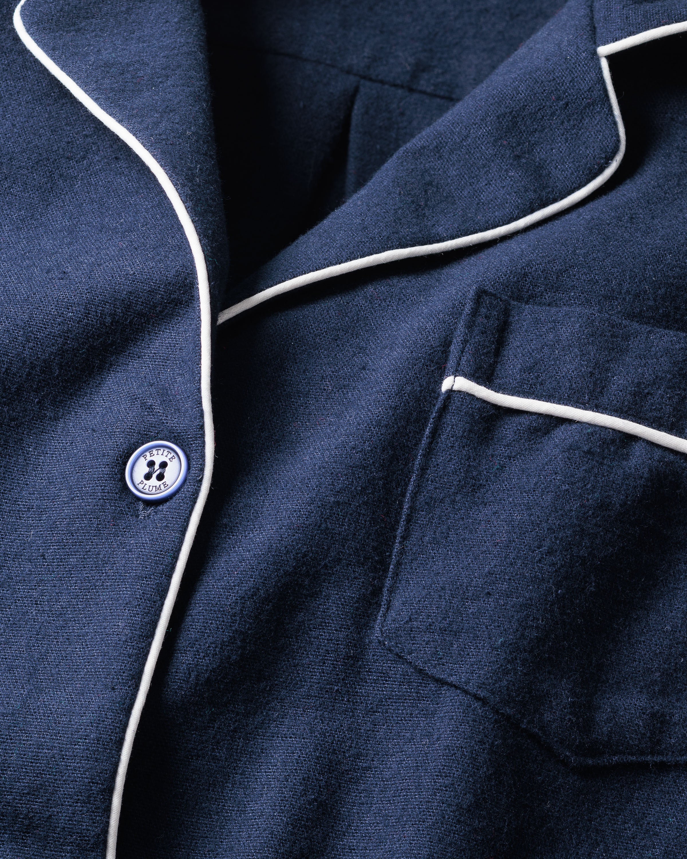 Close-up of Petite Plumes Mens Flannel Pajama Set in Navy: a soft, textured fabric with white piping and a paw-print button by the pocket. Enjoy cozy loungewear vibes with moisture-wicking comfort to keep you dry and snug.