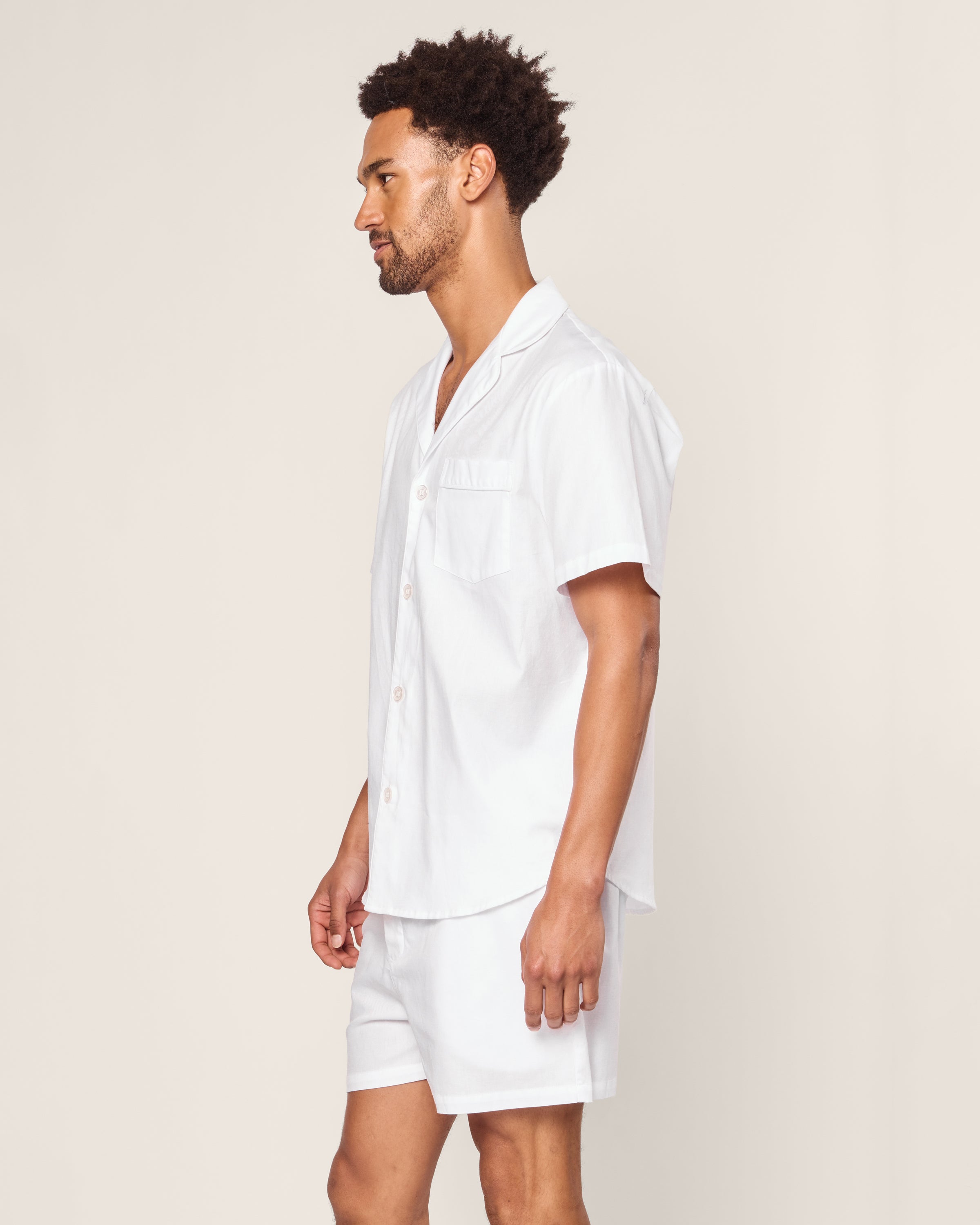 A man stands sideways against a plain background wearing a Mens Twill Pajama Short Set White with White Piping by Petite Plume.