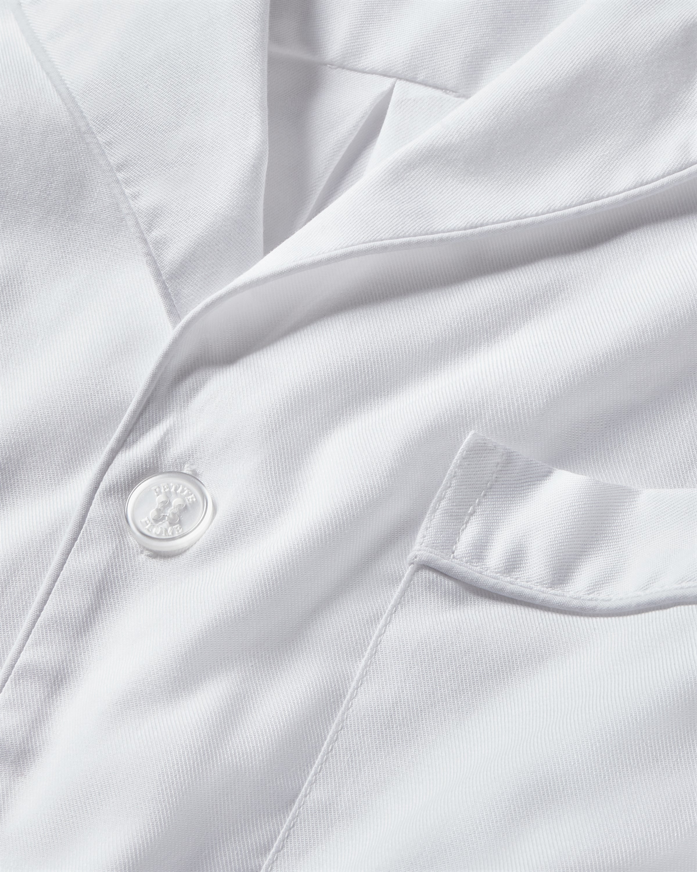 Close-up of the Mens Twill Pajama Short Set by Petite Plume in white with white piping, featuring a textured, yarn-dyed shirt that highlights luxurious softness through its buttons, visible pocket, and collar.