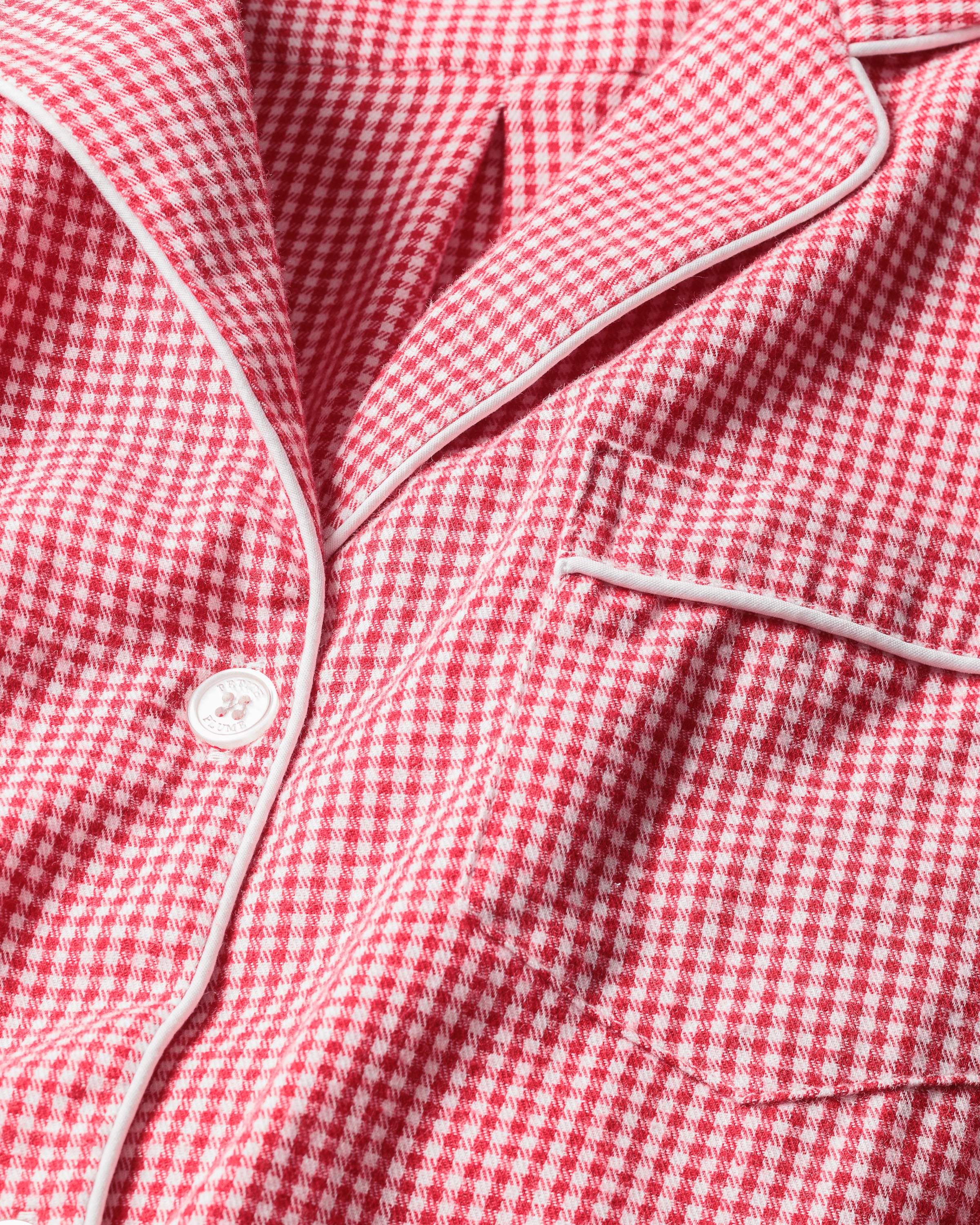 A close-up of Petite Plumes Mens Flannel Pajama Set in Red Mini Gingham reveals the finest quality cotton fabric with white piping, a button, and a pocket, exemplifying classic pajama set design.