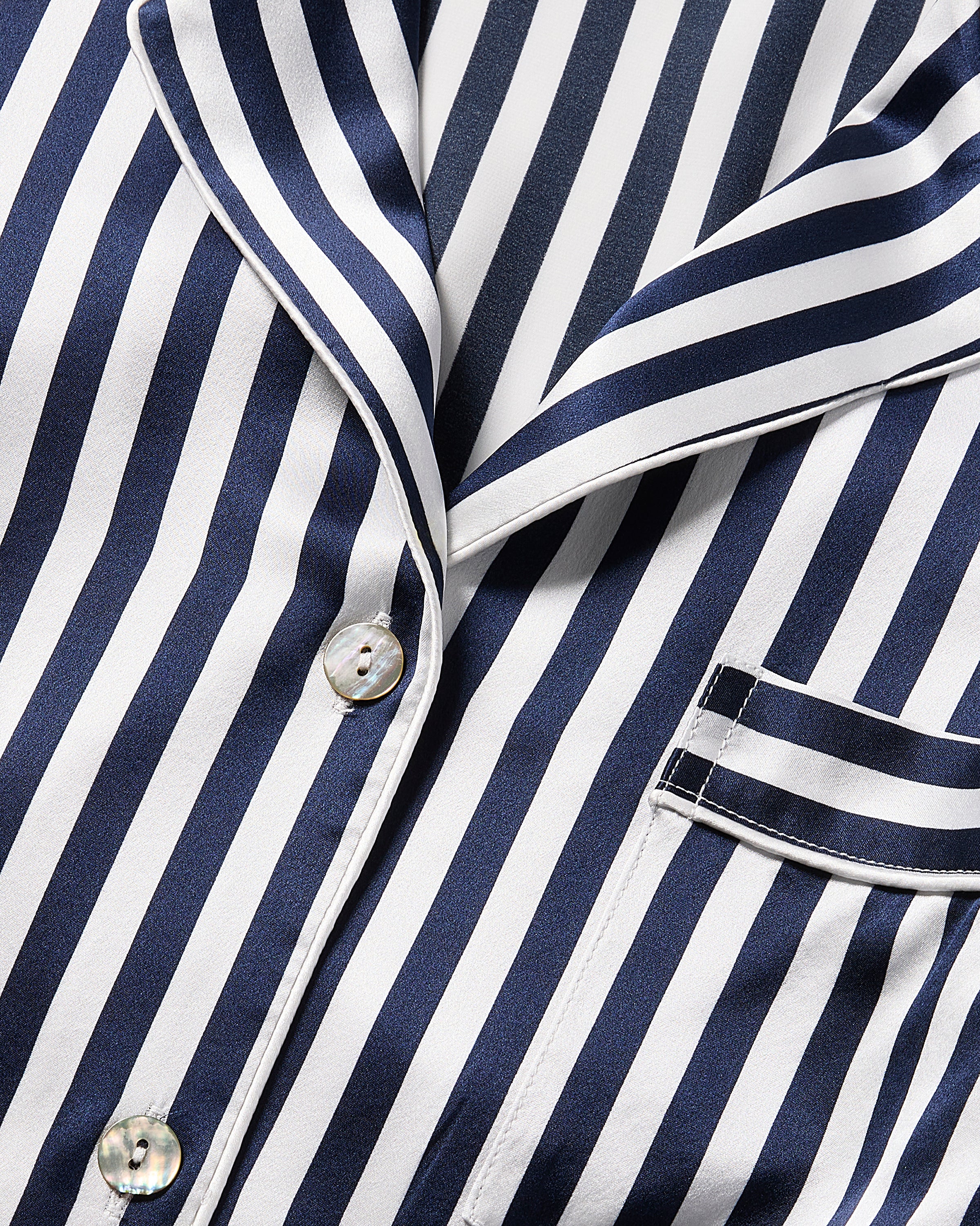 Close-up of Petite Plumes Mens Silk Pajama Set in Navy Bengal Stripe featuring a buttoned front, front pocket, and contrasting trim on the collar and pocket. Made from mulberry silk, it offers a shiny, smooth look for ultimate comfort and elegance.