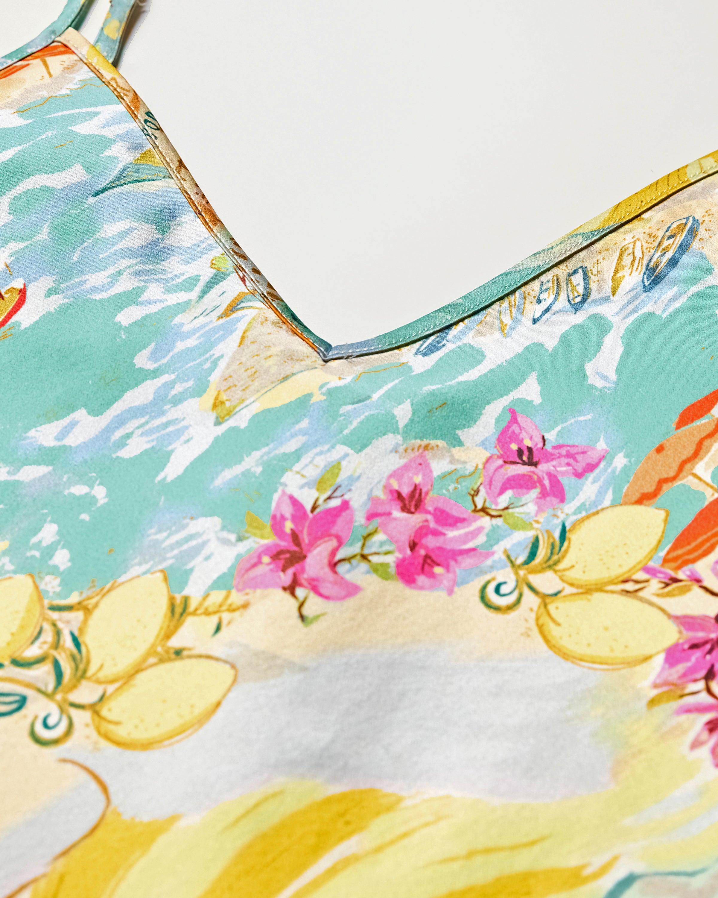 Close-up of Petite Plumes Womens Silk Cami Short Set in La Dolce Vita, showcasing a vibrant floral and ocean-inspired design. Featuring pink flowers, yellow leaves, and blue water-like patterns for a summery look with a V-shaped neckline. Ideal for luxury sleepwear.