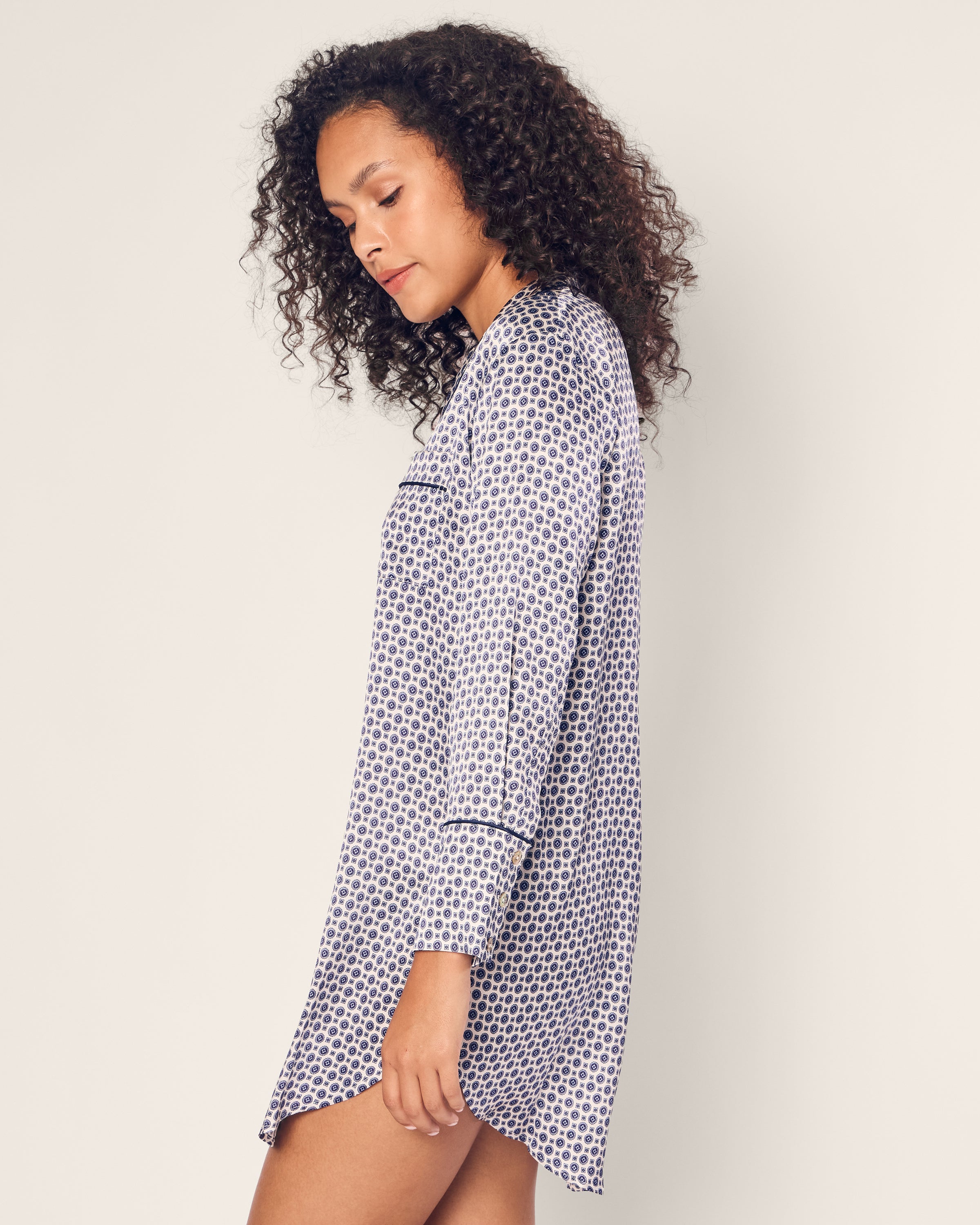 A woman with curly hair models the Petite Plume Womens Silk Nightshirt in Navy Foulard. She stands sideways, eyes gently closed, against a plain background.