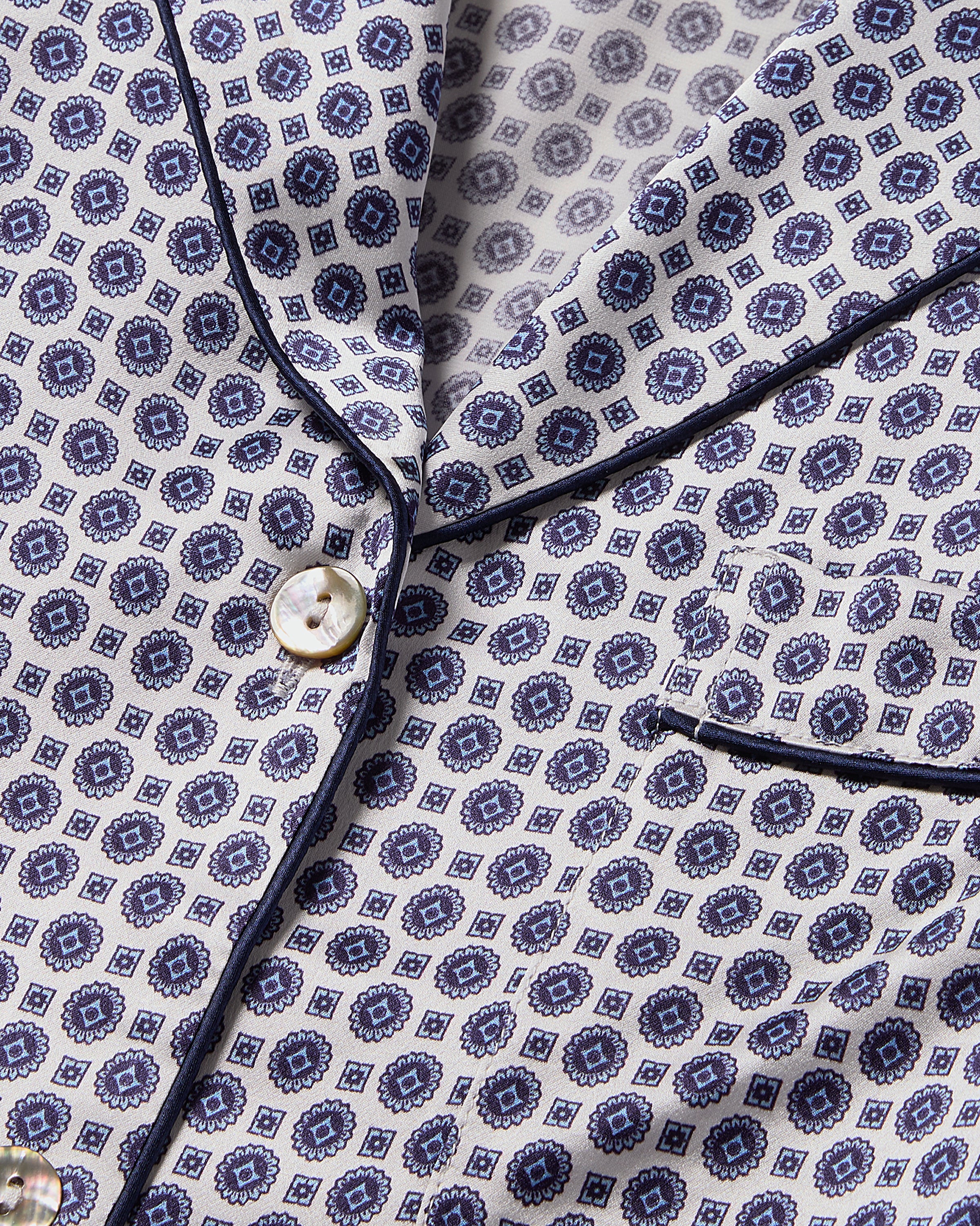 This exquisite close-up highlights Petite Plume’s Womens Silk Nightshirt in Navy Foulard, crafted from luxurious Mulberry silk with dark and light blue geometric shapes on a white background. It features elegant white buttons and refined black piping on the edges and pocket.