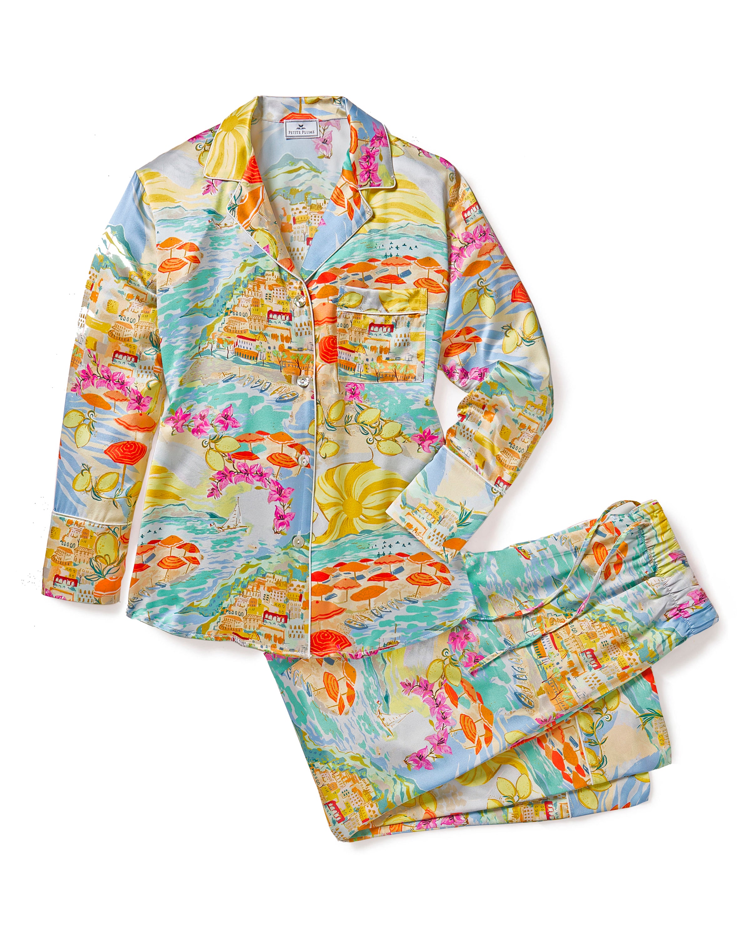 The Womens Silk Pajama Set in La Dolce Vita by Petite Plume features a long-sleeve button-up shirt and pants adorned with a vibrant coastal print of buildings, ocean waves, sailboats, and umbrellas in blue, orange, yellow, and pink—ideal for elevating your sleepwear collection.