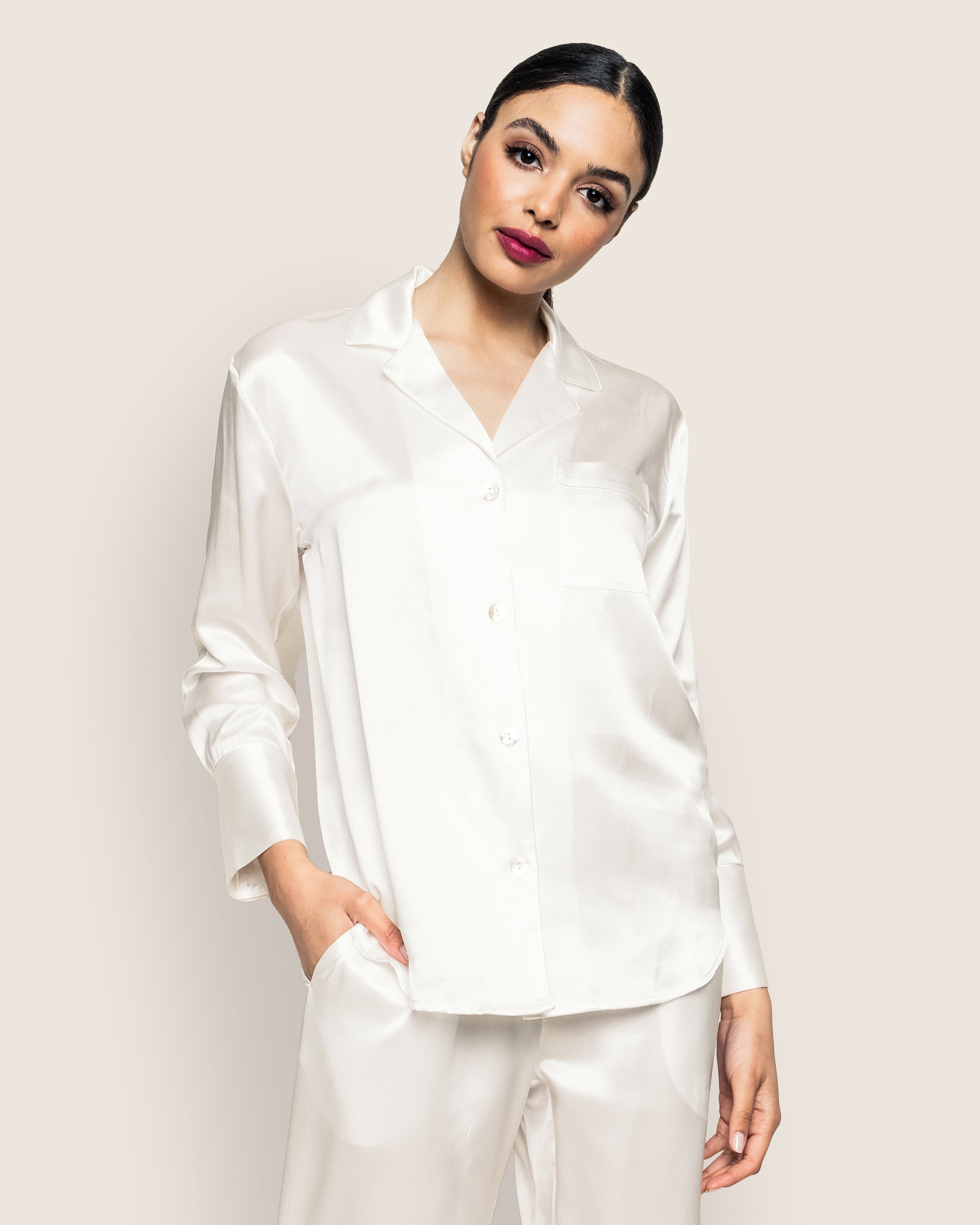 Elegantly dressed in Petite Plumes luxurious Womens Silk Pajama Set in White, the person poses against a plain background with one hand casually tucked in their pocket.