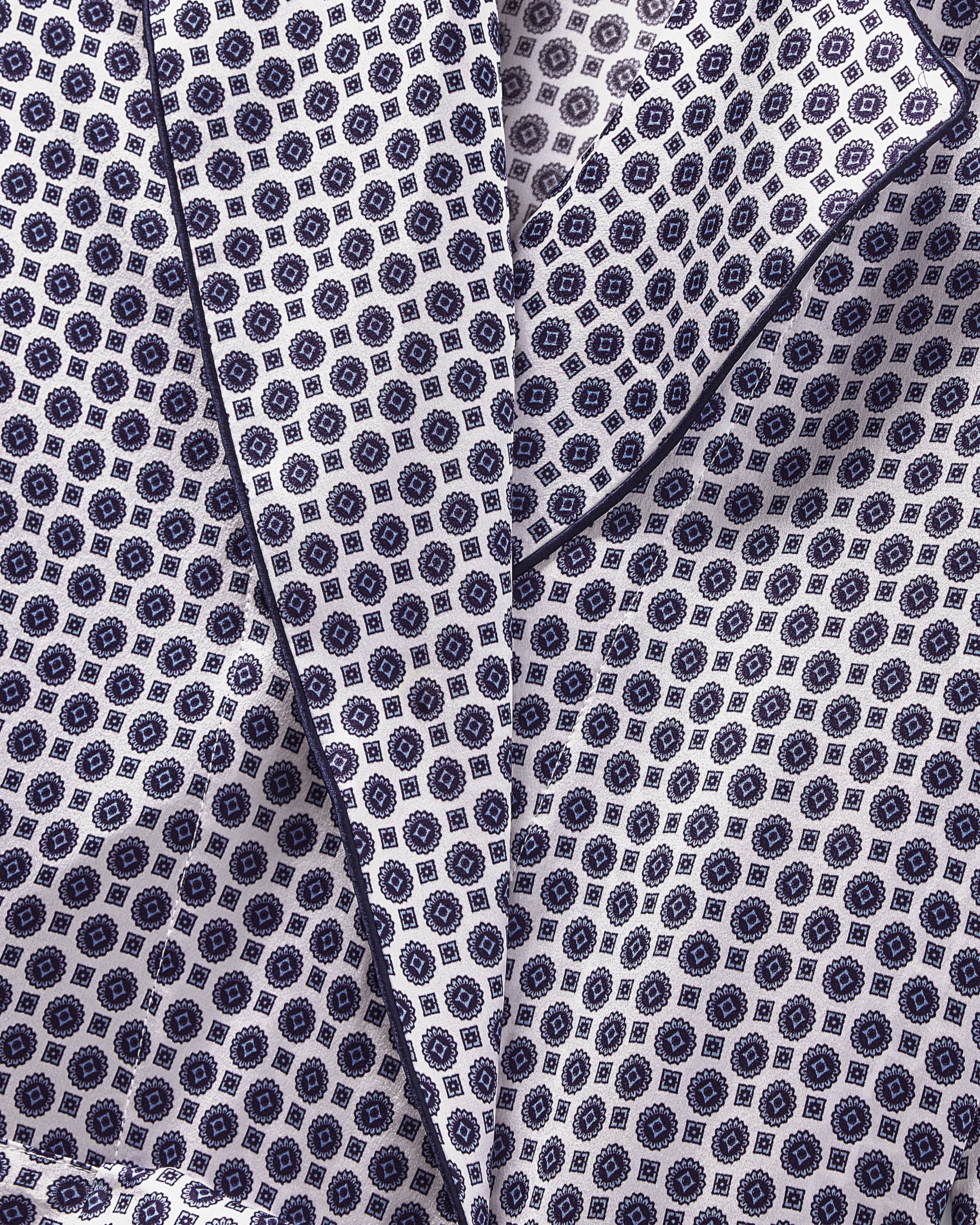 A close-up view of the Navy Foulard patterned silk fabric from Petite Plume shows a geometric design in blue and white. The mulberry silk, folded or draped, creates textured shadows and highlights, ideal for luxurious womens sleepwear like the Womens Silk Robe.