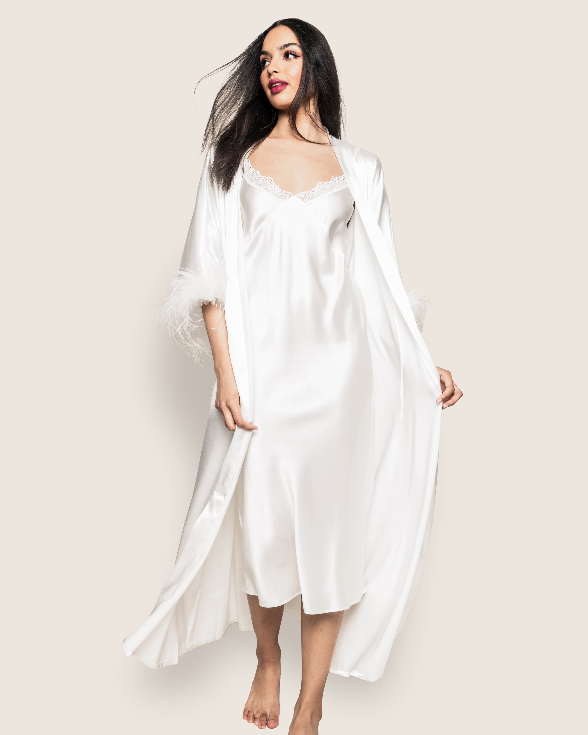 A woman with long dark hair is wearing the Womens Silk Lace Cosette Nightgown in White by Petite Plume, barefoot and gracefully posing against a plain background, embodying elegant sleepwear.