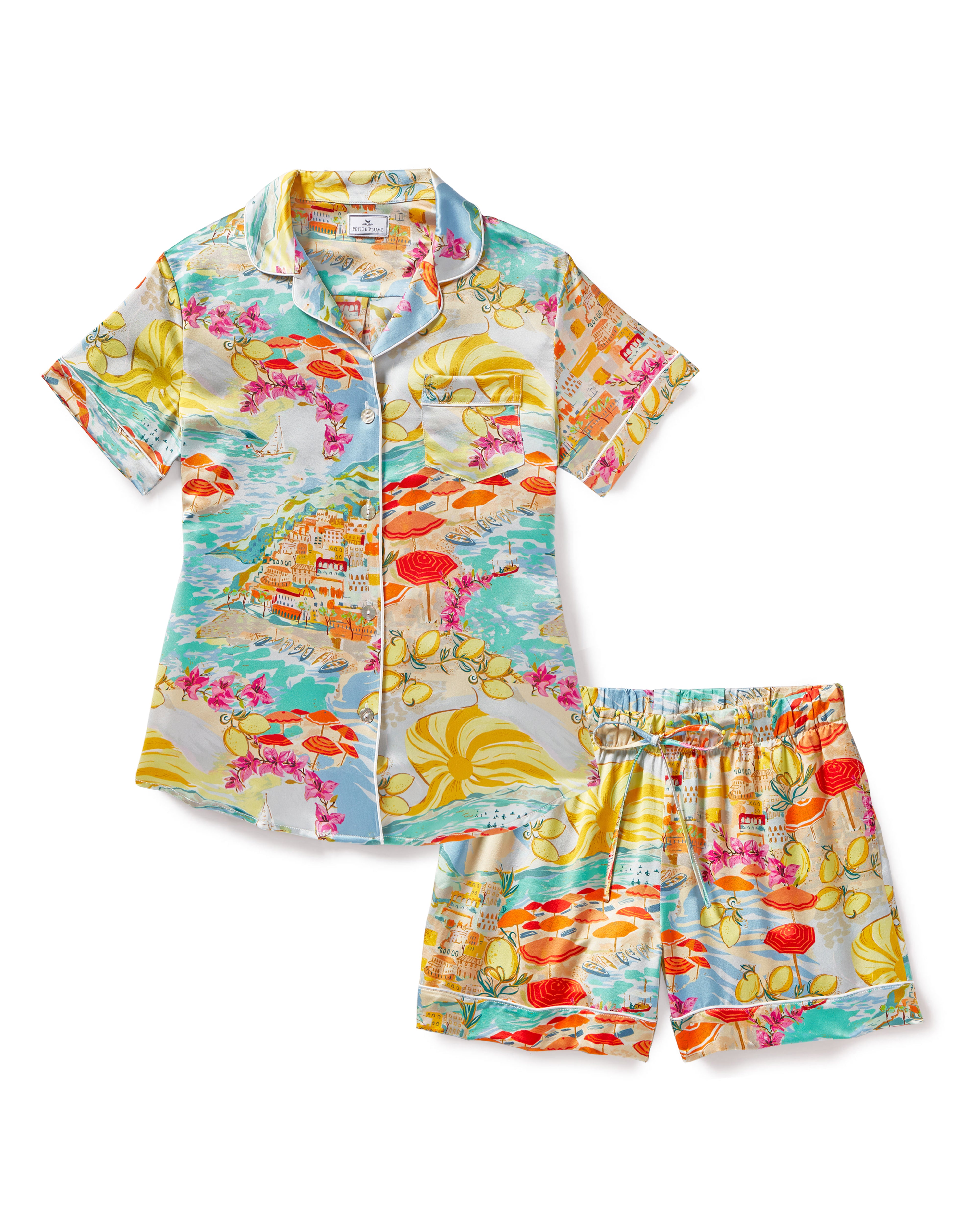 The Petite Plume Womens Silk Short Set in La Dolce Vita is a colorful pajama set featuring a short-sleeved button-up shirt and matching shorts. It showcases vibrant designs with Italian seaside scenes, floral motifs, and swirling water patterns in shades of blue, orange, pink, and yellow.