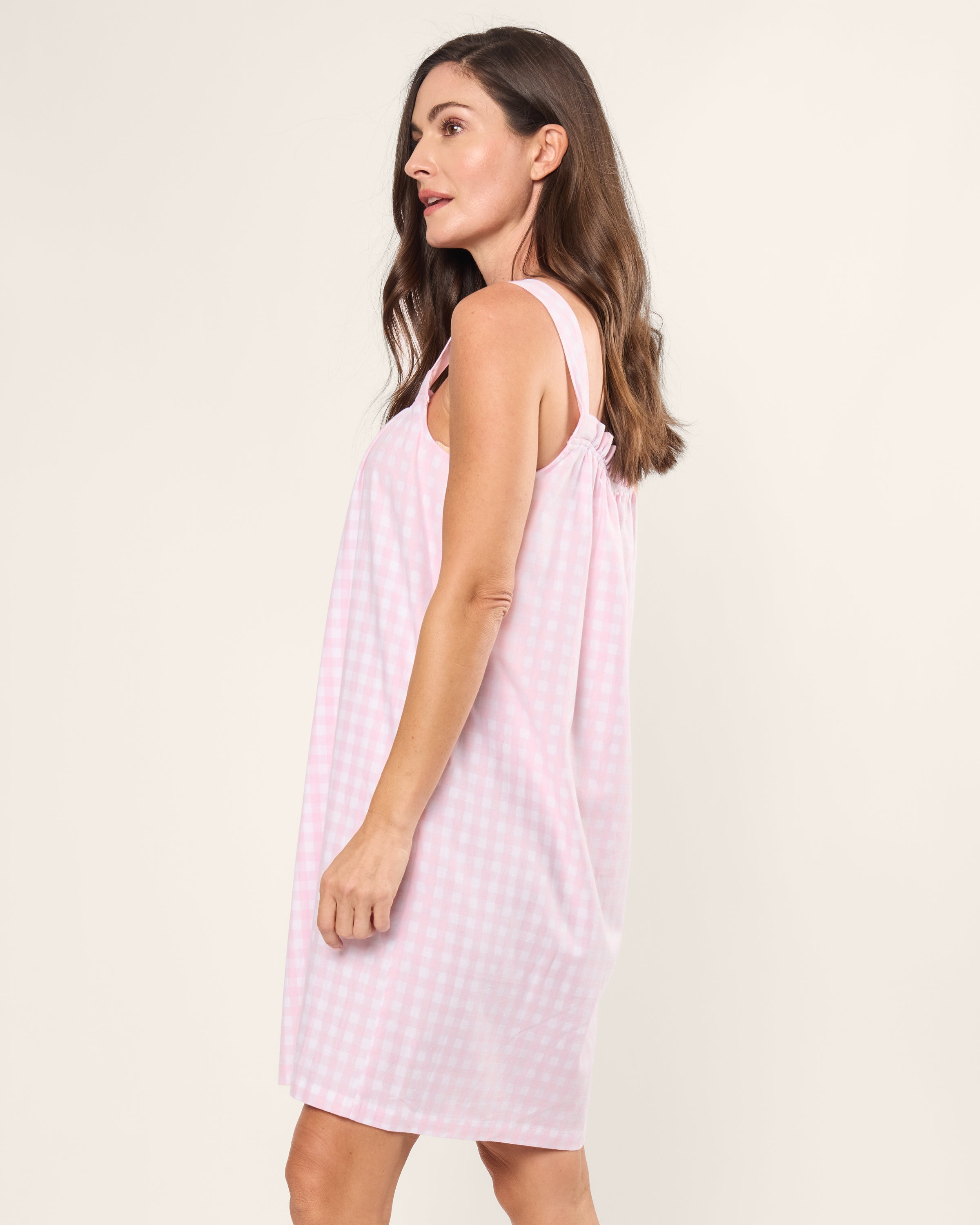 A woman with long brown hair wears the Womens Twill Annabelle Nightgown in Pink Gingham by Petite Plume, facing sideways against a plain white background and exuding the charm of luxury sleepwear.