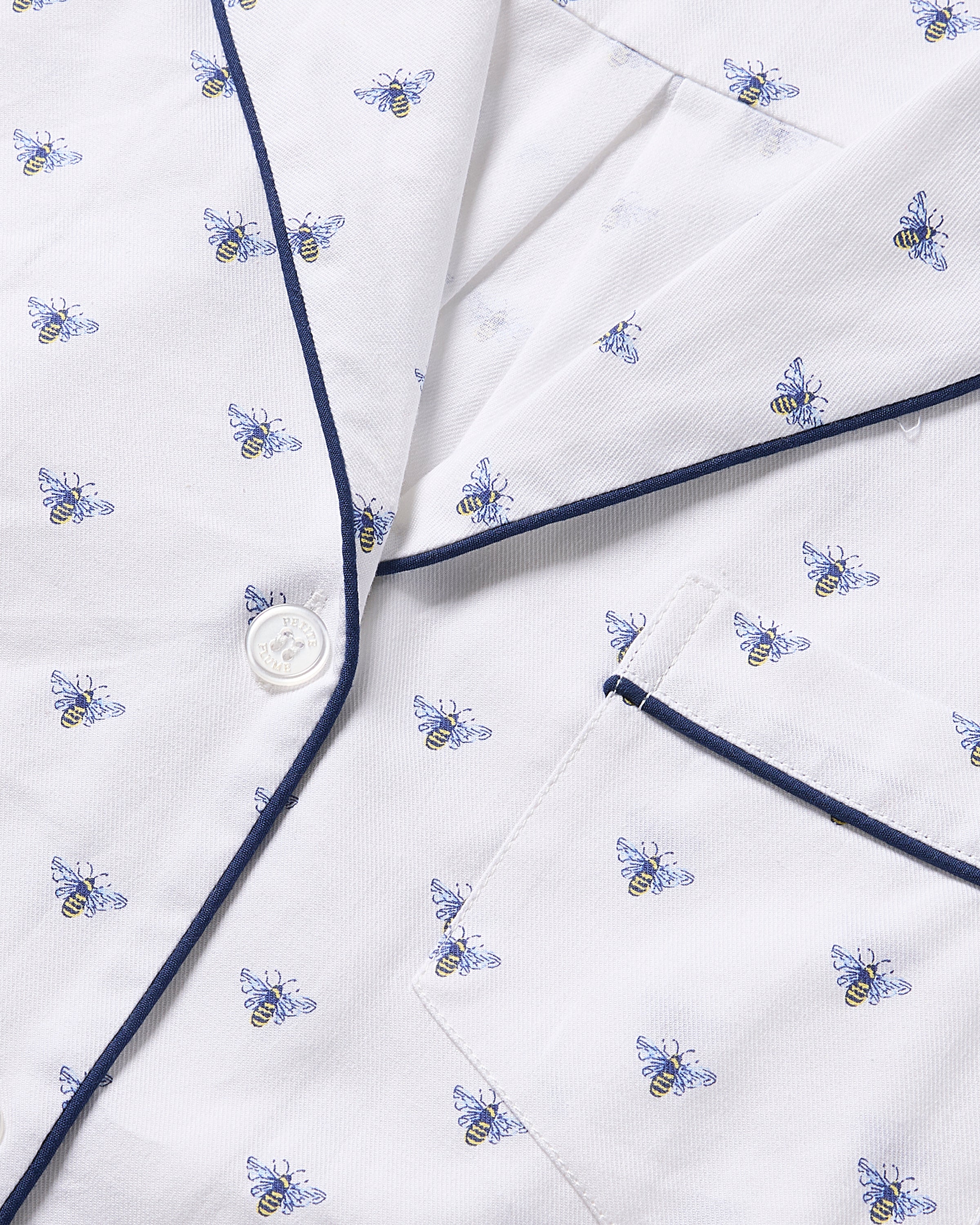 Close-up of the Womens Twill Long Sleeve Short Set in Buzzing Bees by Petite Plume. Luxurious fabric with blue and yellow bees, navy piping on collar and pocket, white button on left. The soft texture promises irresistible comfort.