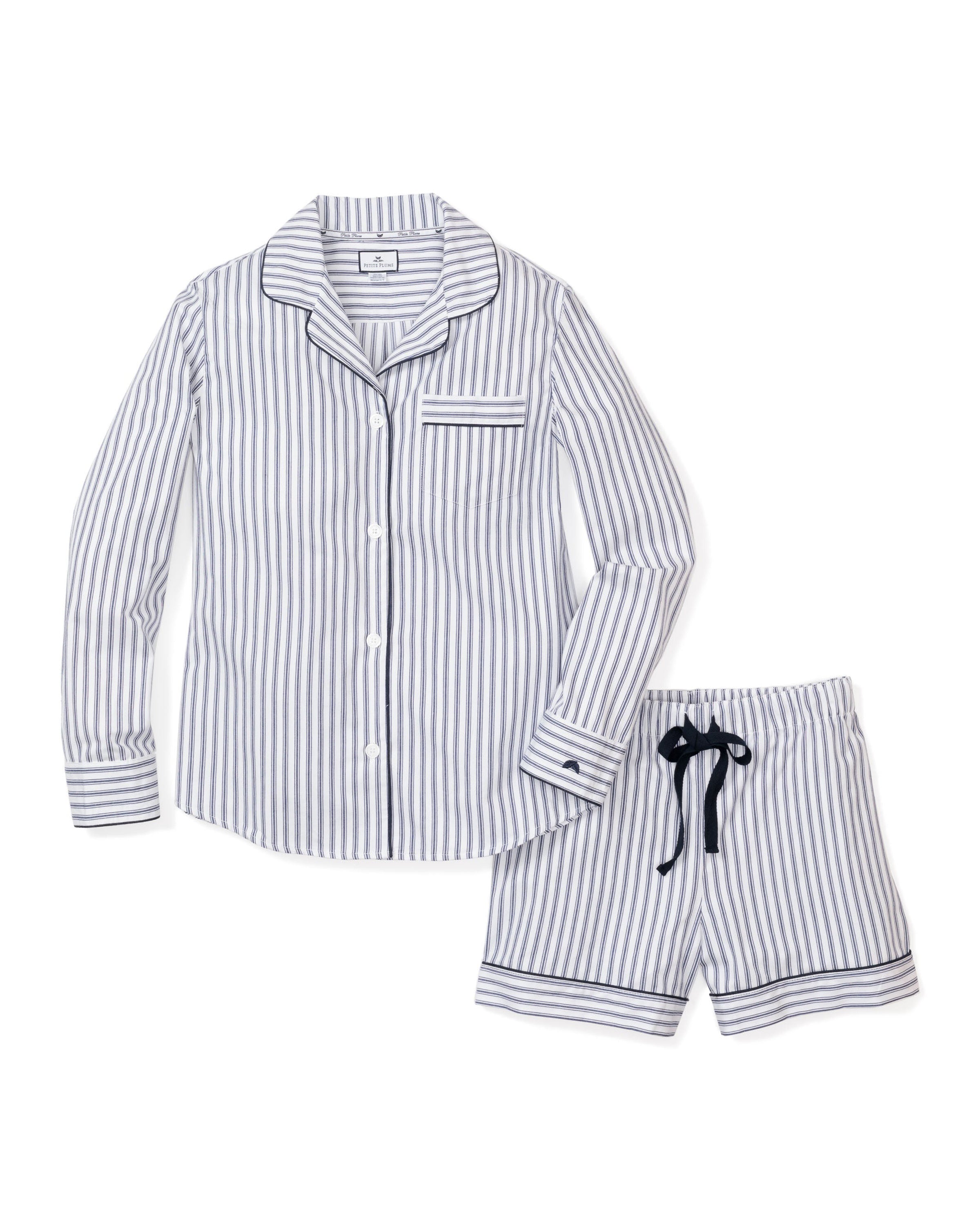 The Womens Twill Long Sleeve Short Set in Navy French Ticking from Petite Plume features elegant blue and white vertical stripes, a button-up top with a collar and chest pocket, and shorts with a black drawstring. Made from 100% cotton twill, this set offers classic style and comfort.