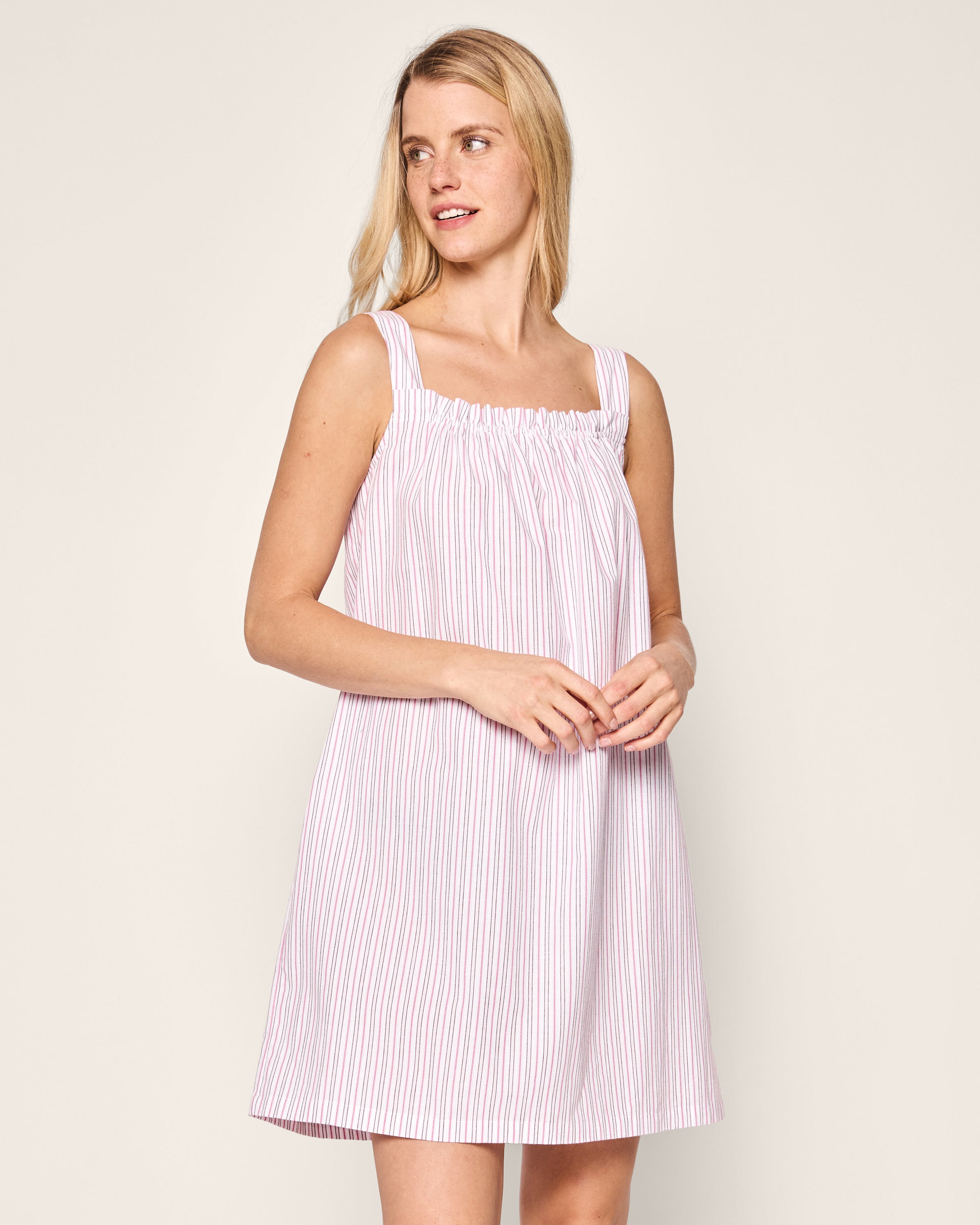 A woman in a Petite Plume Womens Twill Annabelle Nightgown with the Blush Boulevard print stands against a neutral background. She has long blonde hair, looks off to the side with a slight smile, and gently clasps her hands in front.