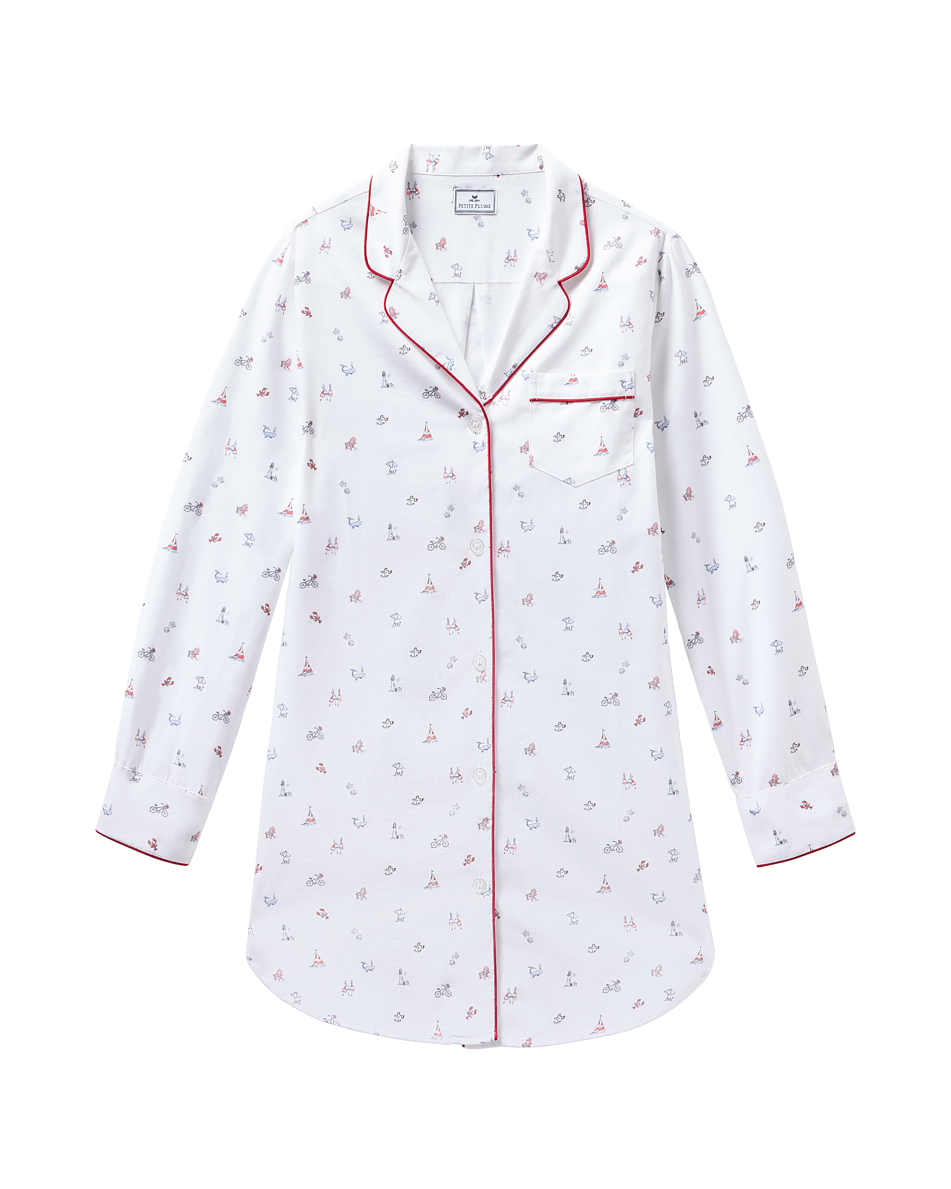 The Womens Twill Nightshirt in Coastal Charms by Petite Plume features a white long-sleeve design with a red and blue sailboat pattern. Made from cotton twill, it includes red piping on the collar, cuffs, and pocket edges, plus a left-side breast pocket for added style.