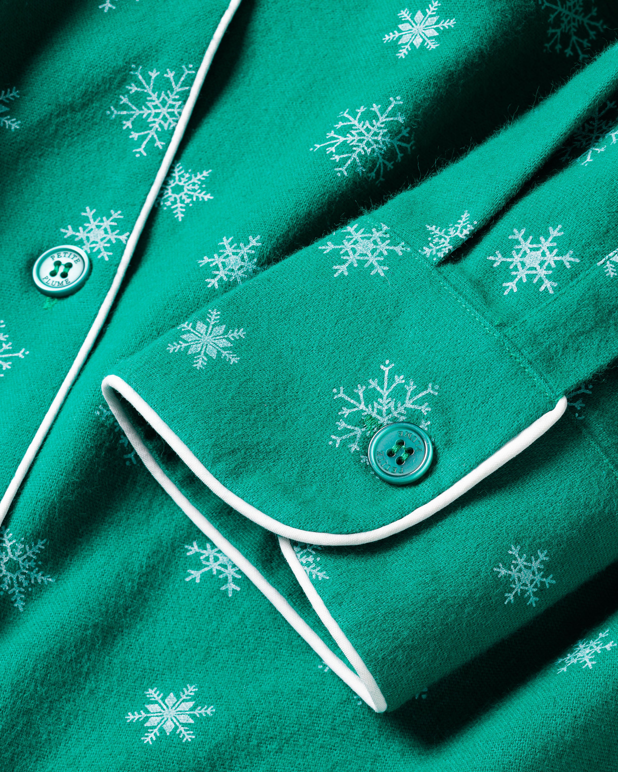 Close-up of Petite Plume’s Women’s Flannel Pajama Set in Emerald Wonderland, featuring luxury cotton with a green and white snowflake pattern. These pajamas boast buttoned cuffs with emerald buttons and elegant white piping—ideal for cozy winter nights.