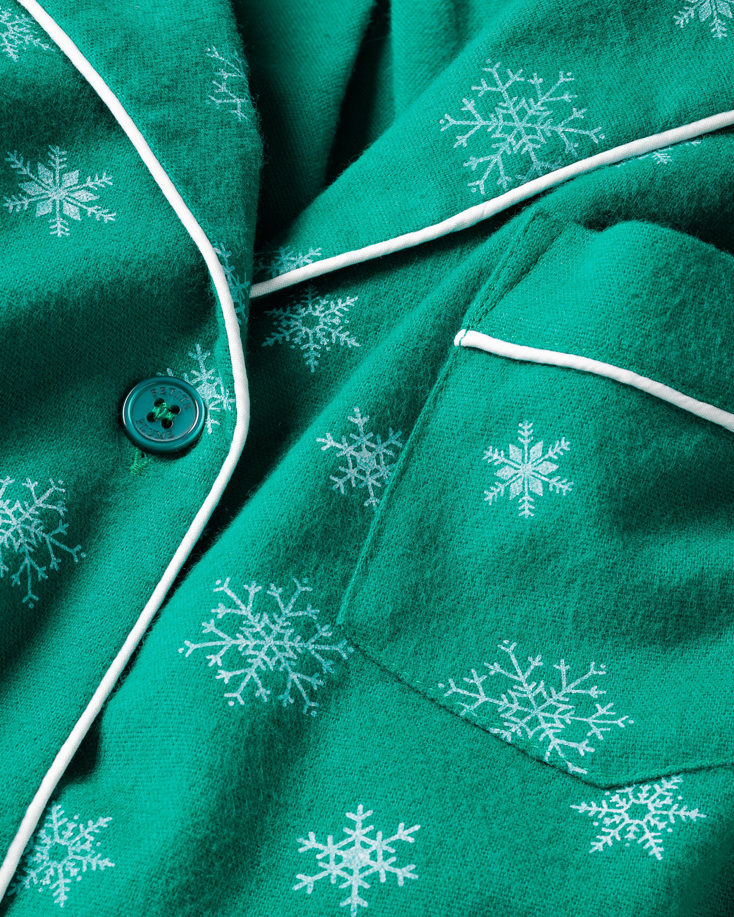 Close-up of the Womens Flannel Pajama Set in Emerald Wonderland by Petite Plume, featuring emerald green fabric with white snowflakes and piping. A green button and matching pocket details add to its soft, cozy texture—ideal luxury cotton sleepwear for chilly winter nights.