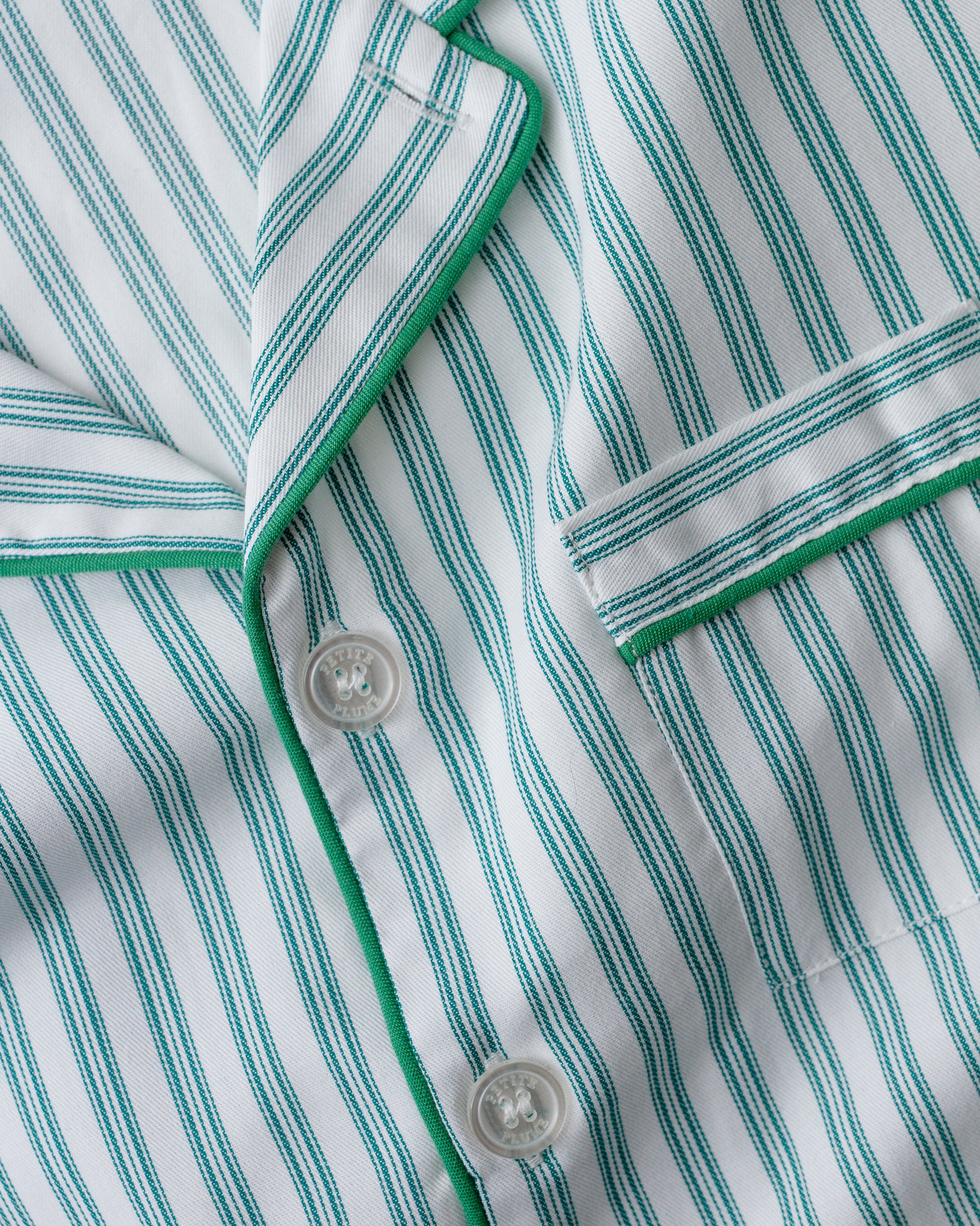 Close-up of Petite Plumes Womens Twill Pajama Set in Emerald Ticking: a cotton pajama with vertical white and teal stripes, accented by green piping, white buttons, and a pocket. The cozy garment features a moisture-wicking weave for added comfort.