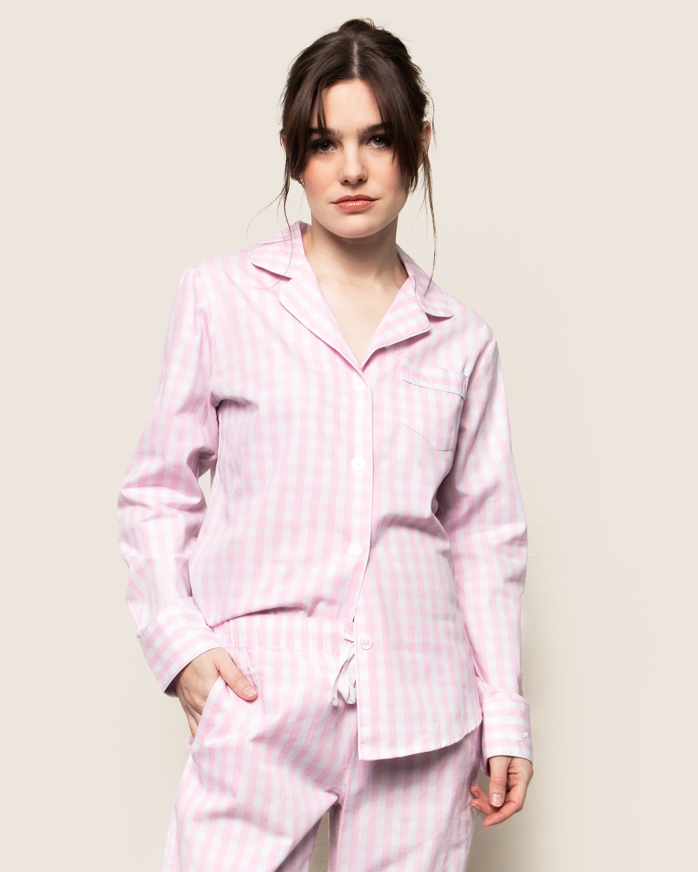 A person wearing Petite Plumes Womens Twill Pajama Set in Pink Gingham, with hands in pockets, stands against a plain off-white background.