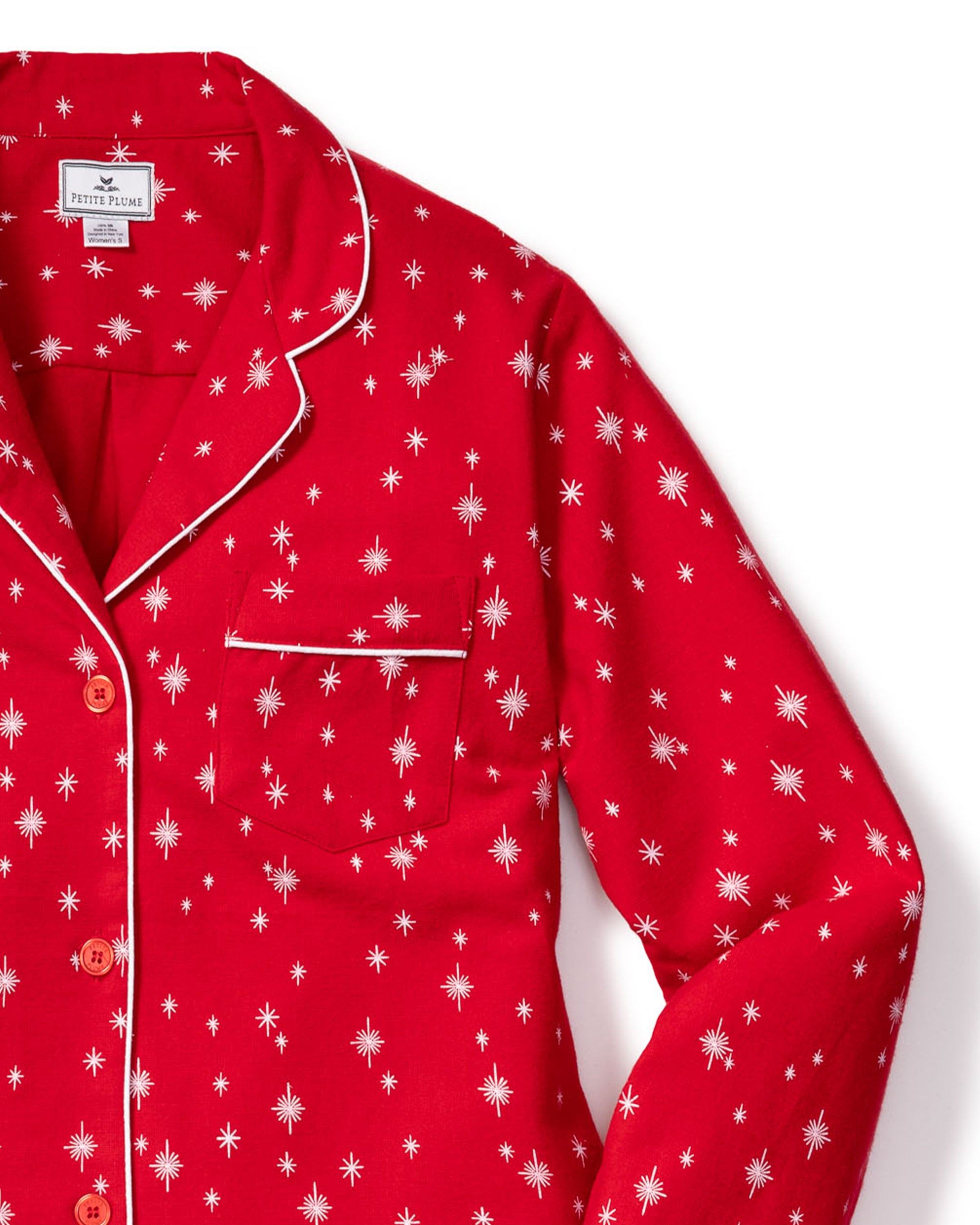 The Womens Flannel Pajama Set in Starry Night by Petite Plume features a cozy pajama top with a red design, white star patterns, and piping. Made from soft cotton sleepwear fabric, it includes a button-down front and chest pocket with matching white trim on the collar.