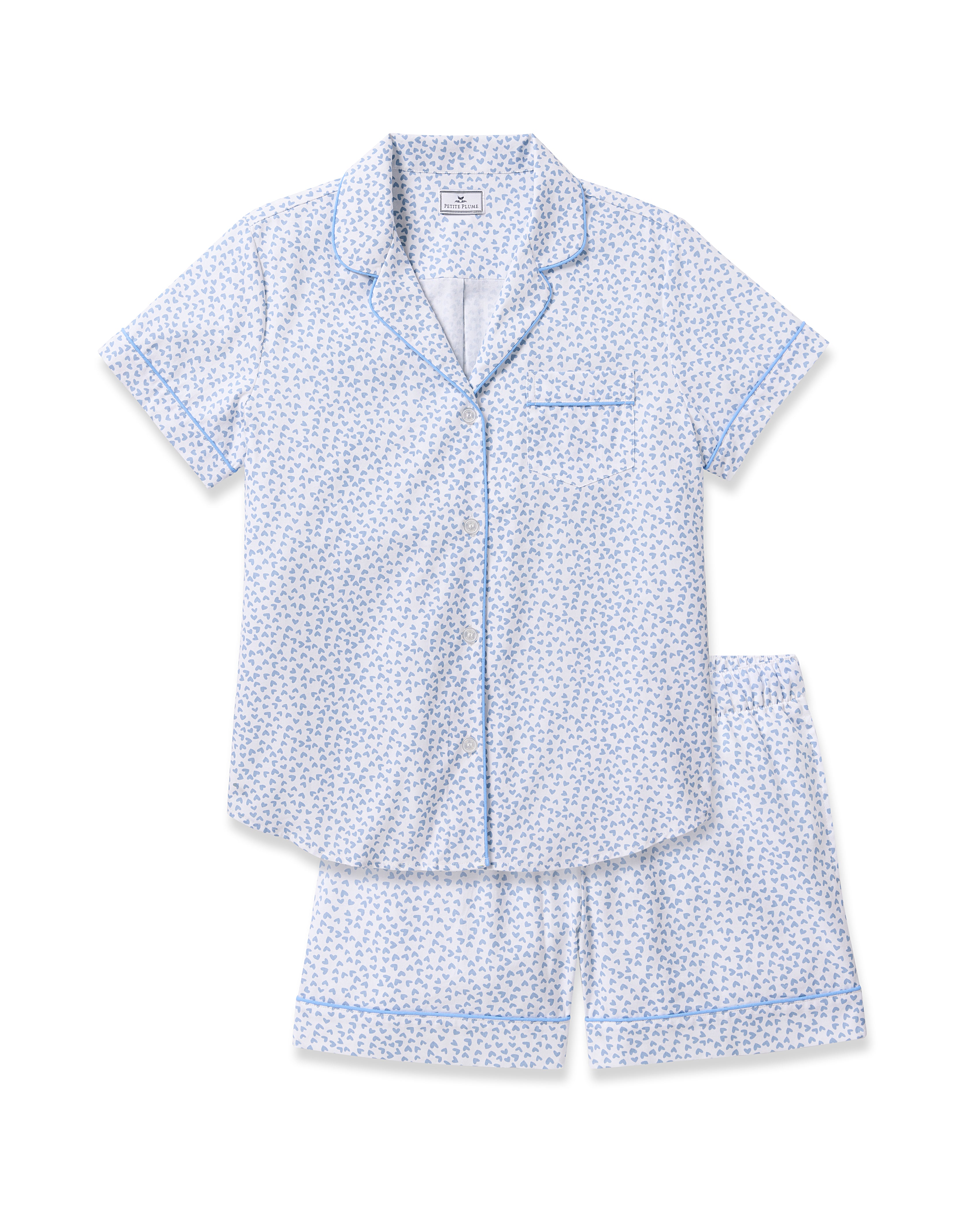 The Womens Twill Short Sleeve Short Set in Bluehearts by Petite Plume is a luxury pajama ensemble featuring a light blue, short-sleeve cotton set with small floral patterns, blue piping accents, a button-up shirt with a front pocket, and matching shorts.