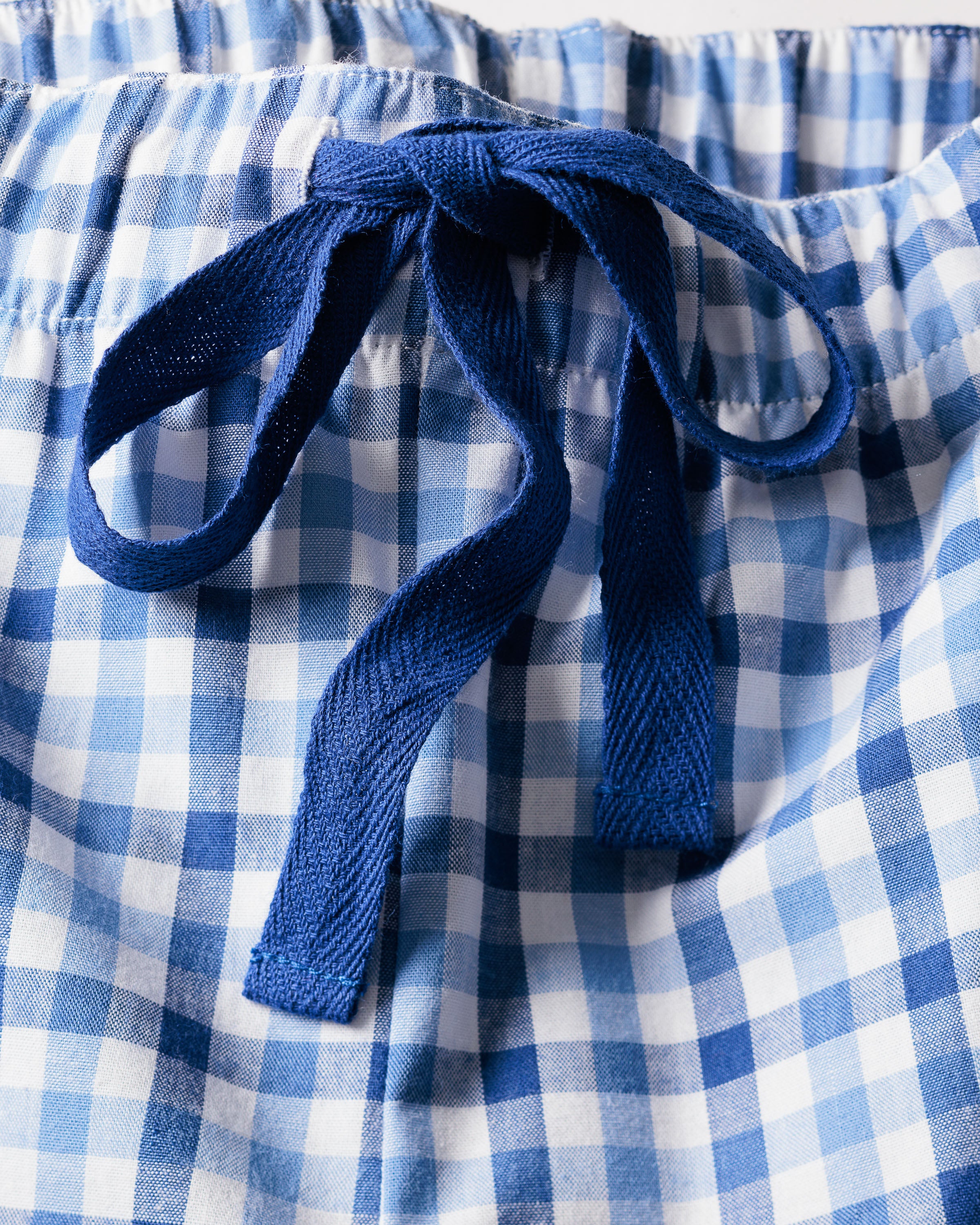 Close-up of the Womens Twill Pajama Short Sleeve Short Set in Royal Blue Gingham by Petite Plume, featuring a blue and white gingham print with a gathered waist and blue drawstring bow. The lightweight, textured fabric exudes luxury sleepwear charm.