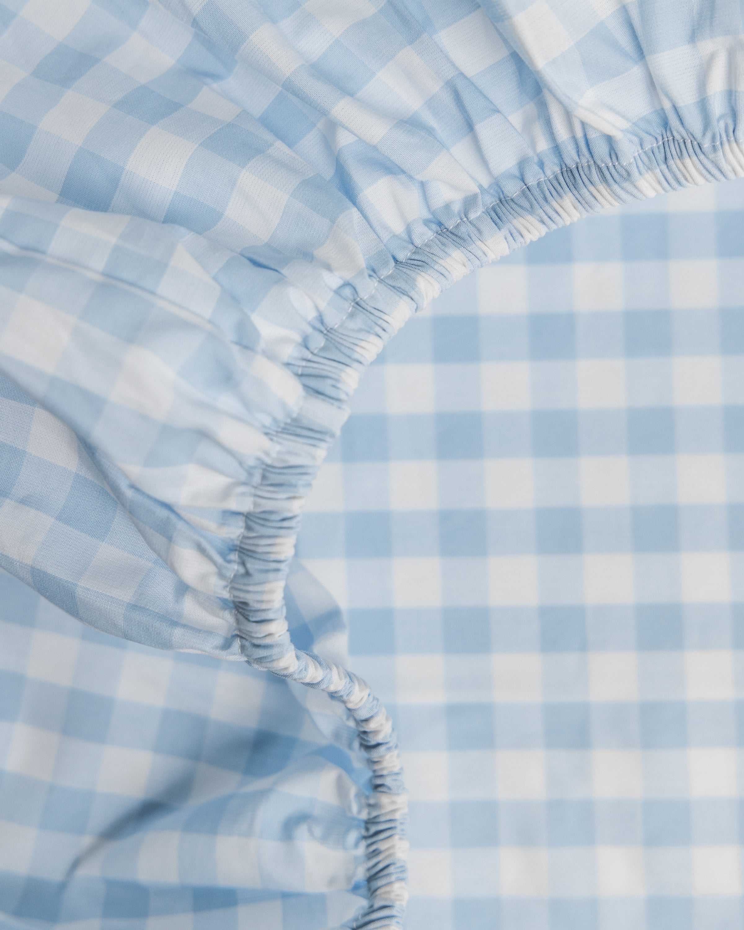 Close-up of the Luxe Premium Light Blue Gingham Crib Sheet by Petite Plume, showcasing its elastic edges and breathable, ultra-soft design.