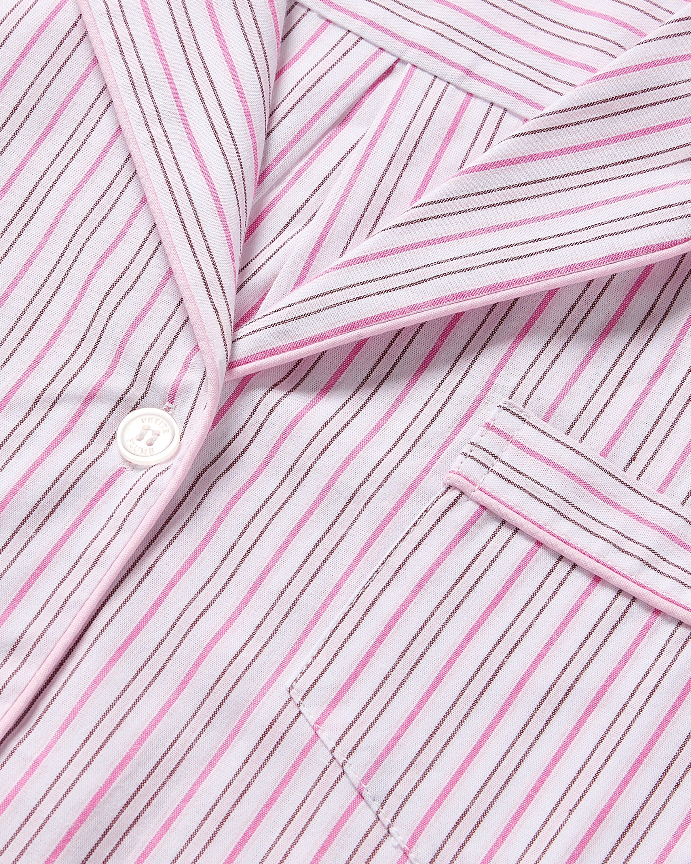 Close-up of the Kids Twill Pajama in Blush Boulevard by Petite Plume, featuring pink, white, and red stripes with a button, collar, and pocket. Made from yarn-dyed cotton for a soft, crisp look.