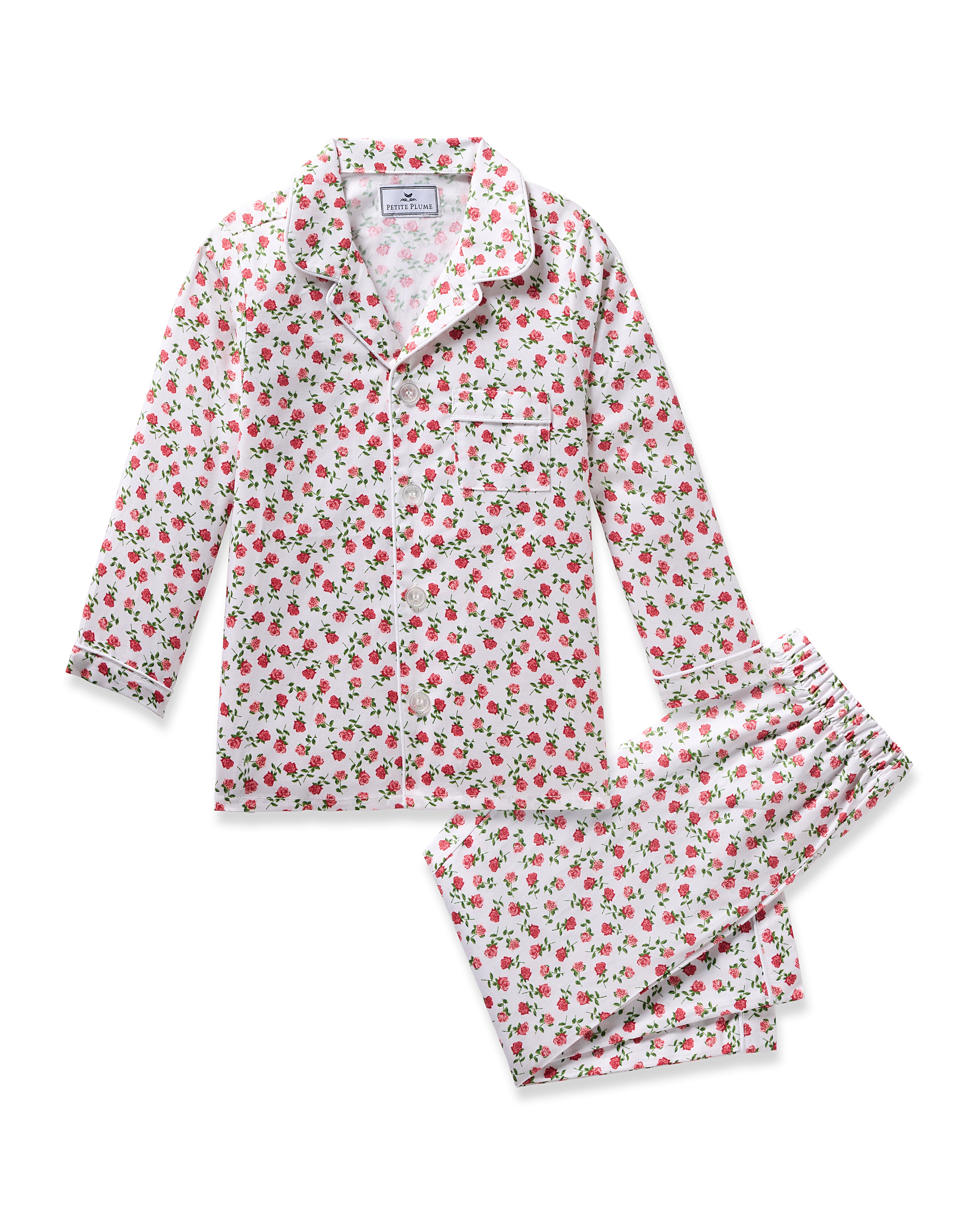 The Kids Twill Pajama in Petite Petals by Petite Plume is a floral set crafted from yarn-dyed cotton. It includes a white long-sleeved shirt and pants with small red roses and green leaves. The shirt features a collar and front buttons for a classic look.